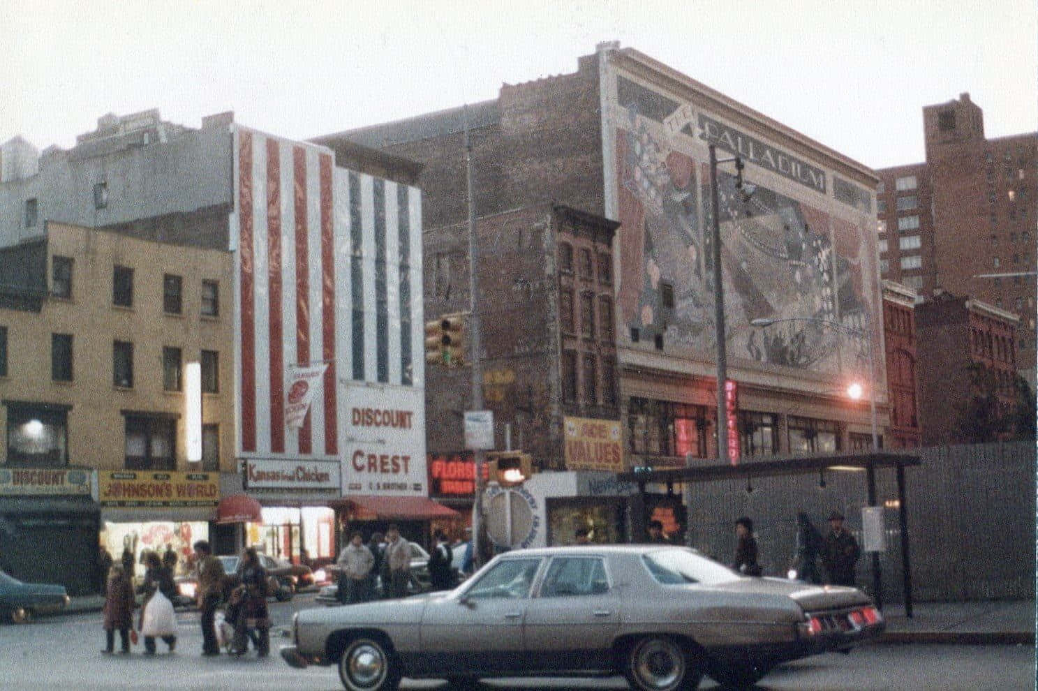 1970年代生動的街景 壁紙 — 復古城市街景，行人正在銀色轎車附近過馬路，磚砌建築上裝飾著褪色的壁畫和復古標誌。