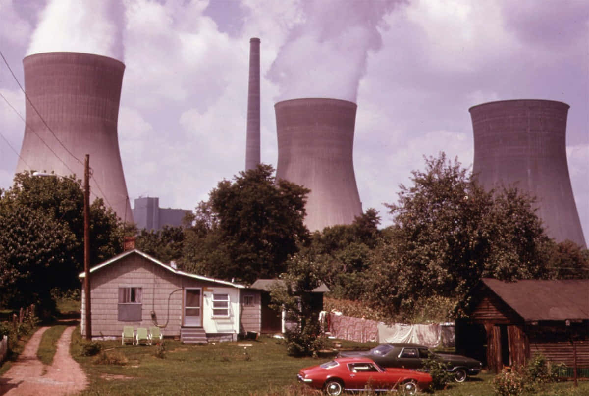 1970年代的搖滾節拍 壁紙 — 一間小屋和經典汽車位於草地庭院中，背景是高聳的核冷卻塔正在排放蒸汽。