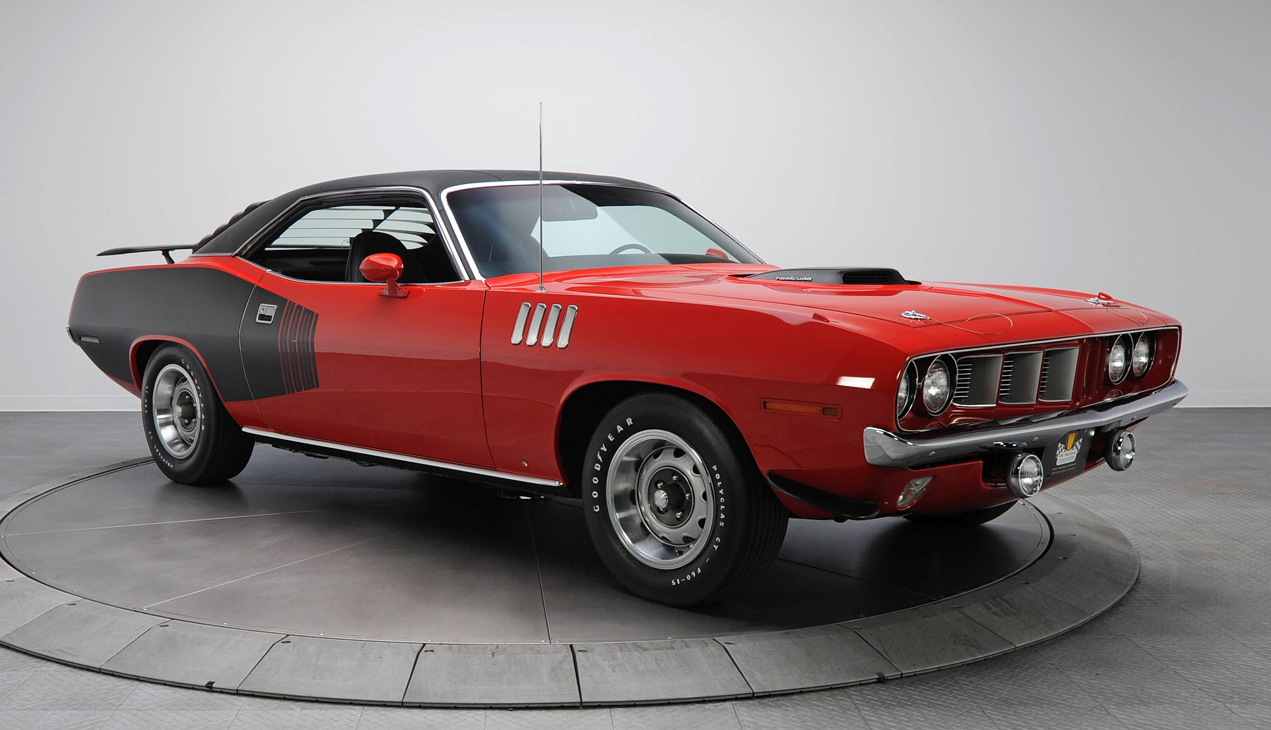 紅黑配色 1971 龐蒂克Hemi Cuda 壁紙 — 一輛引人注目的紅黑配色1970年代肌肉車，帶有鍍鉻裝飾和Goodyear輪胎，停在圓形轉盤上，背景是極簡主義工作室。