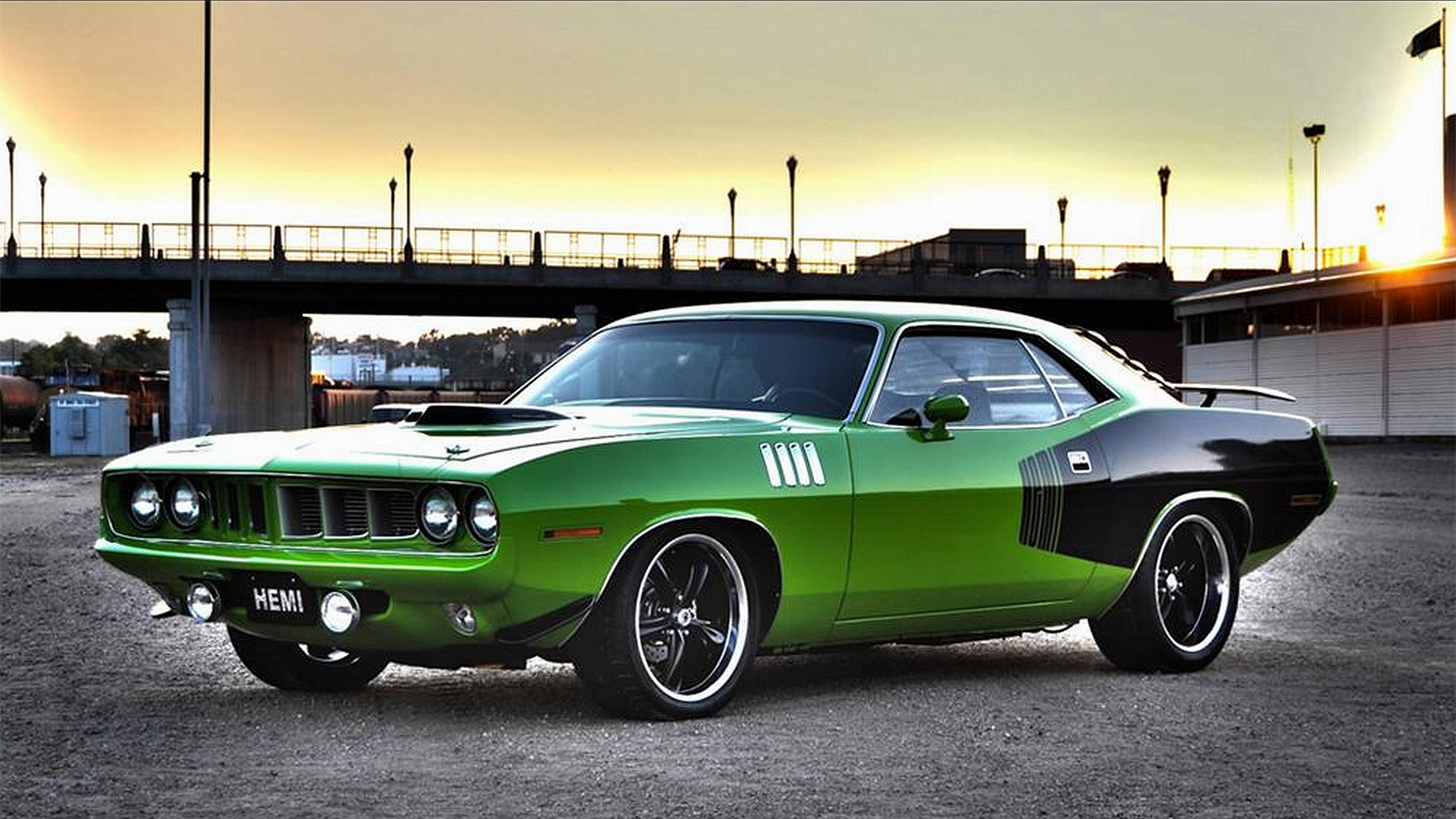 綠色1971年款Plymouth Hemi Barracuda 壁紙 — 一輛充滿活力的綠色經典肌肉車，帶有黑色點綴，停在夕陽下的橋下。