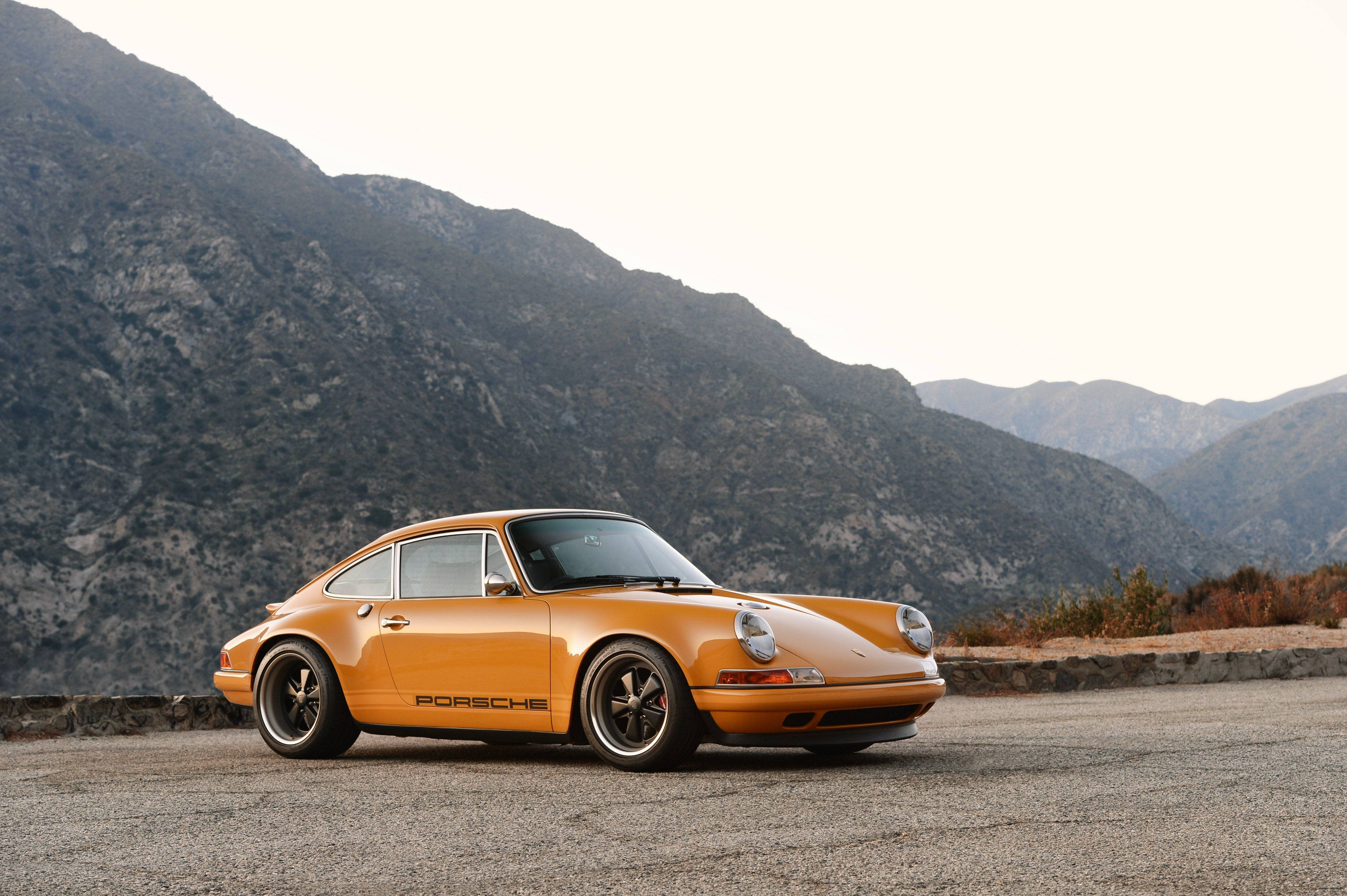 1973年Singer保時捷911 壁紙 — 一輛充滿活力的橙色保時捷911經典跑車停泊在山路上，背景是崎嶇的山峰。