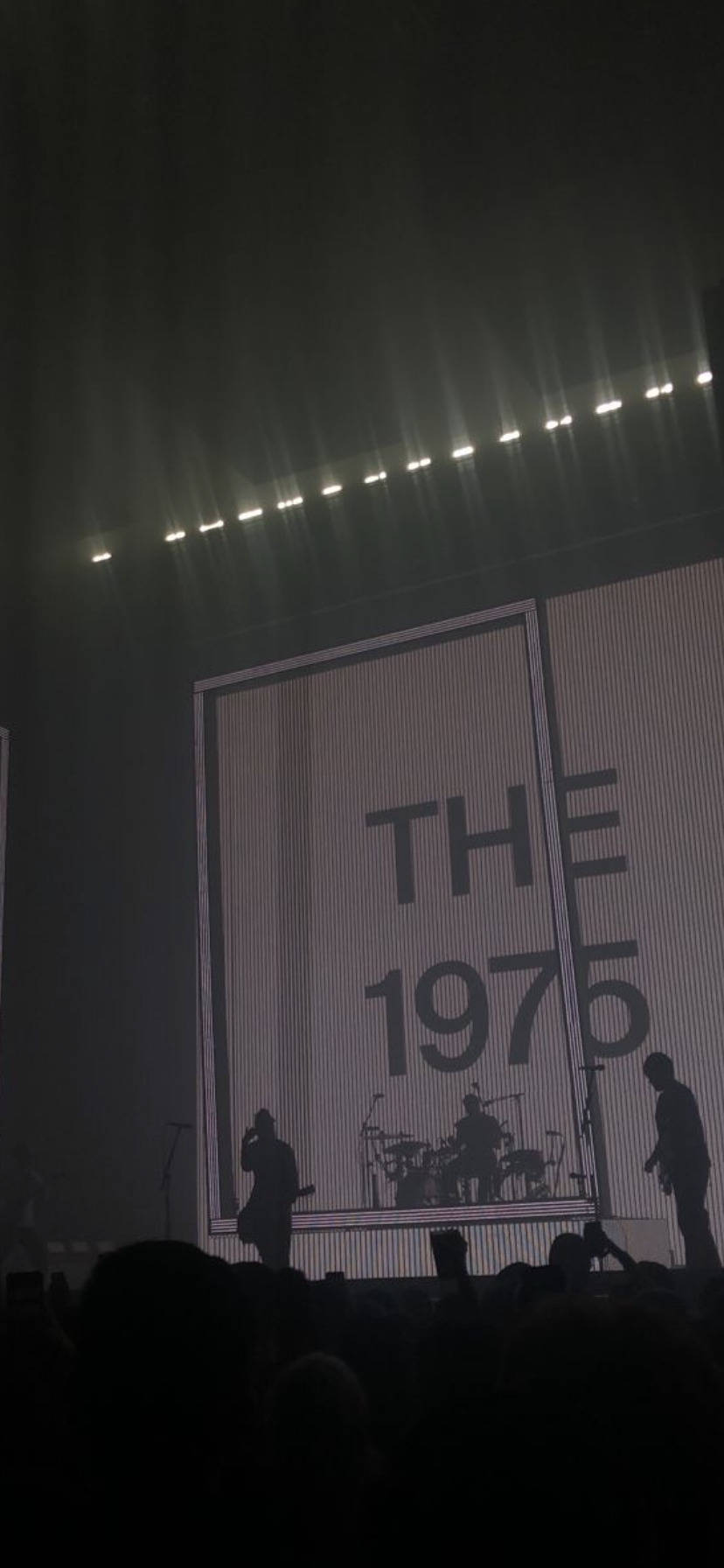剪影音樂家在明亮的燈光下於舞台上表演，屏幕上顯示「THE 1975」。