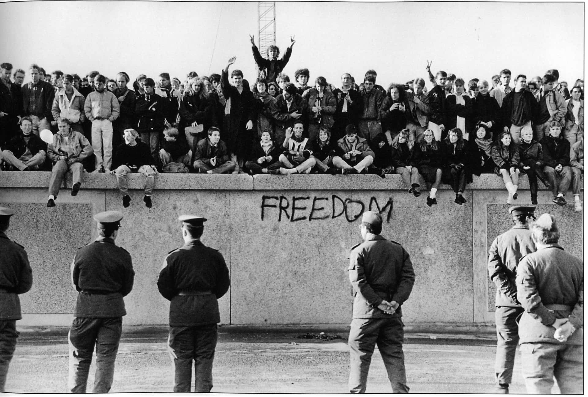 人們坐在帶有「FREEDOM」塗鴉的牆上，士兵站在下方。