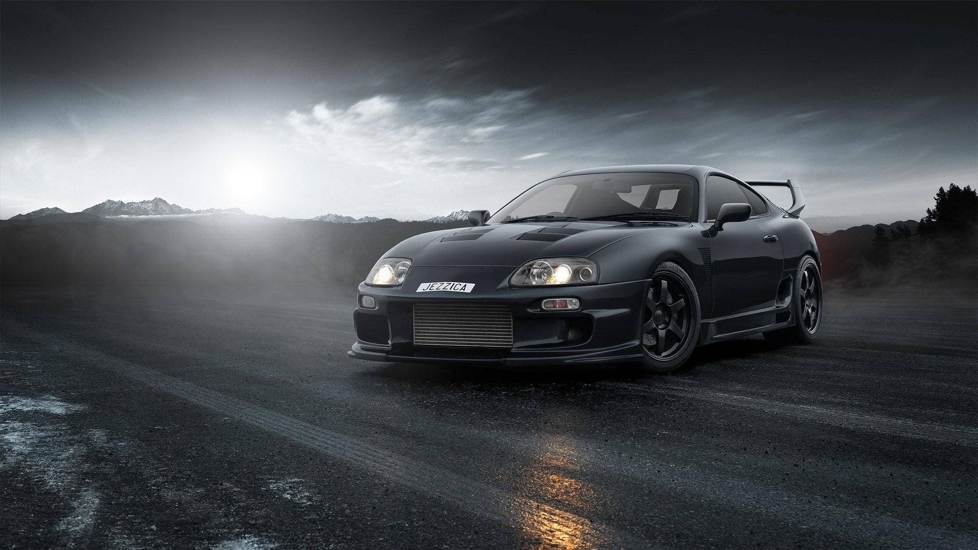 單色1994年豐田Supra Mk4 壁紙 — 一輛時尚的黑色跑車配以發光的車頭燈，在戲劇性的多雲天空下，主宰著霧氣瀰漫的山路。