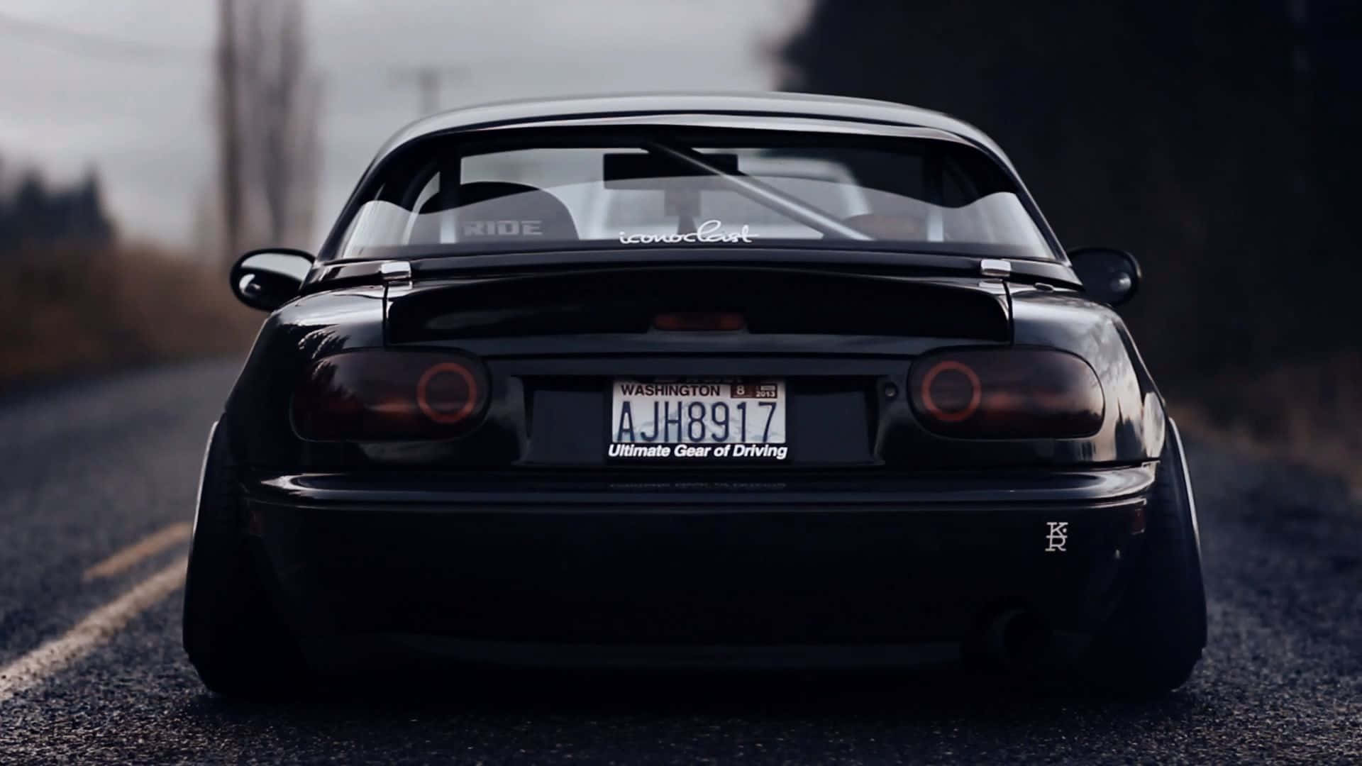 1995年馬自達MX-5 Miata亮面黑色跑車 壁紙 — 一輛配備定制寬體套件的時尚黑色跑車，停泊在霧氣瀰漫的鄉村道路上，尾燈在昏暗的天空下柔和地發光。