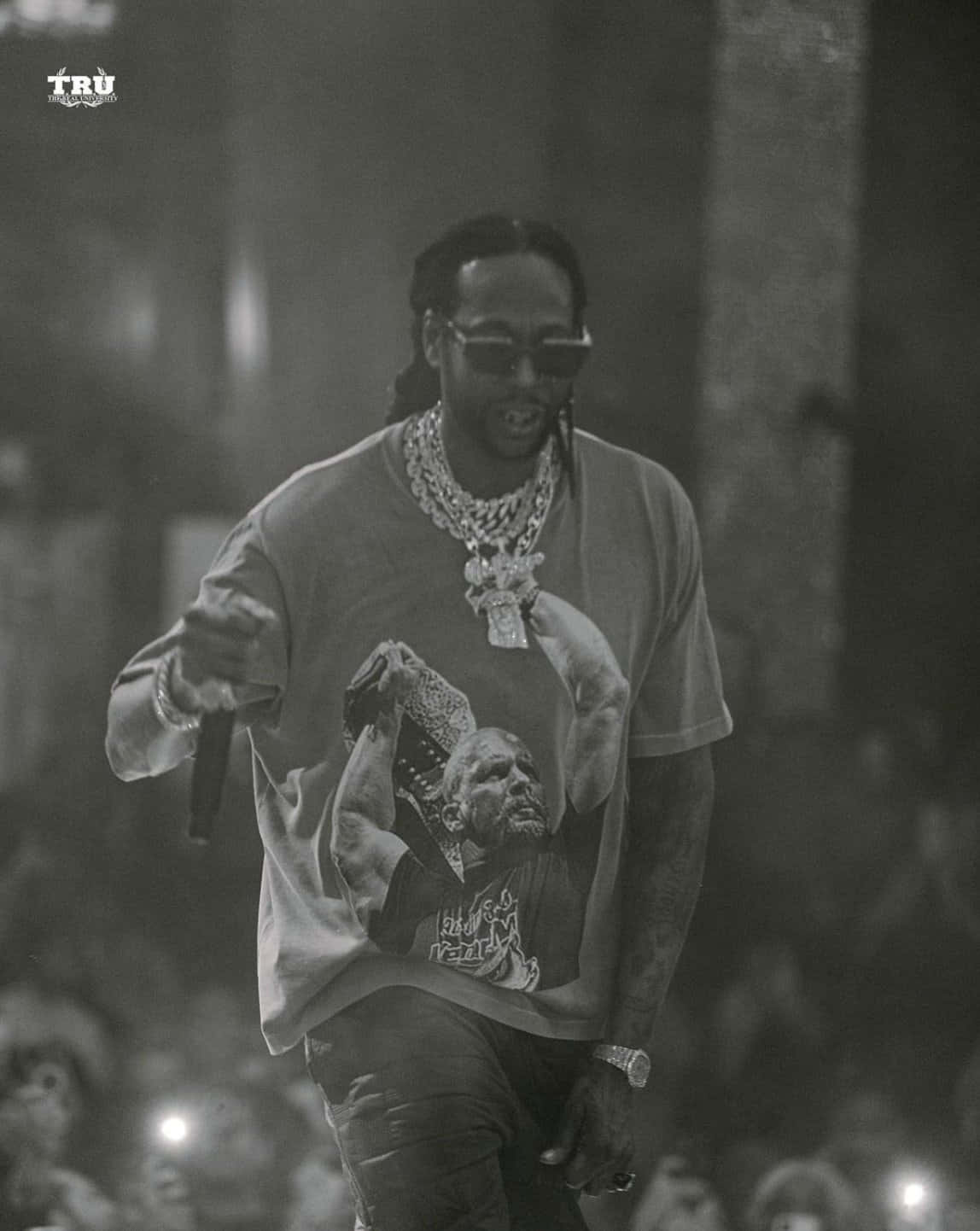 2 Chainz 帶來最強饒舌 壁紙 — 一張黑白照片，一位饒舌歌手在舞台上表演，戴著太陽眼鏡和圖案T恤，背景有群眾。