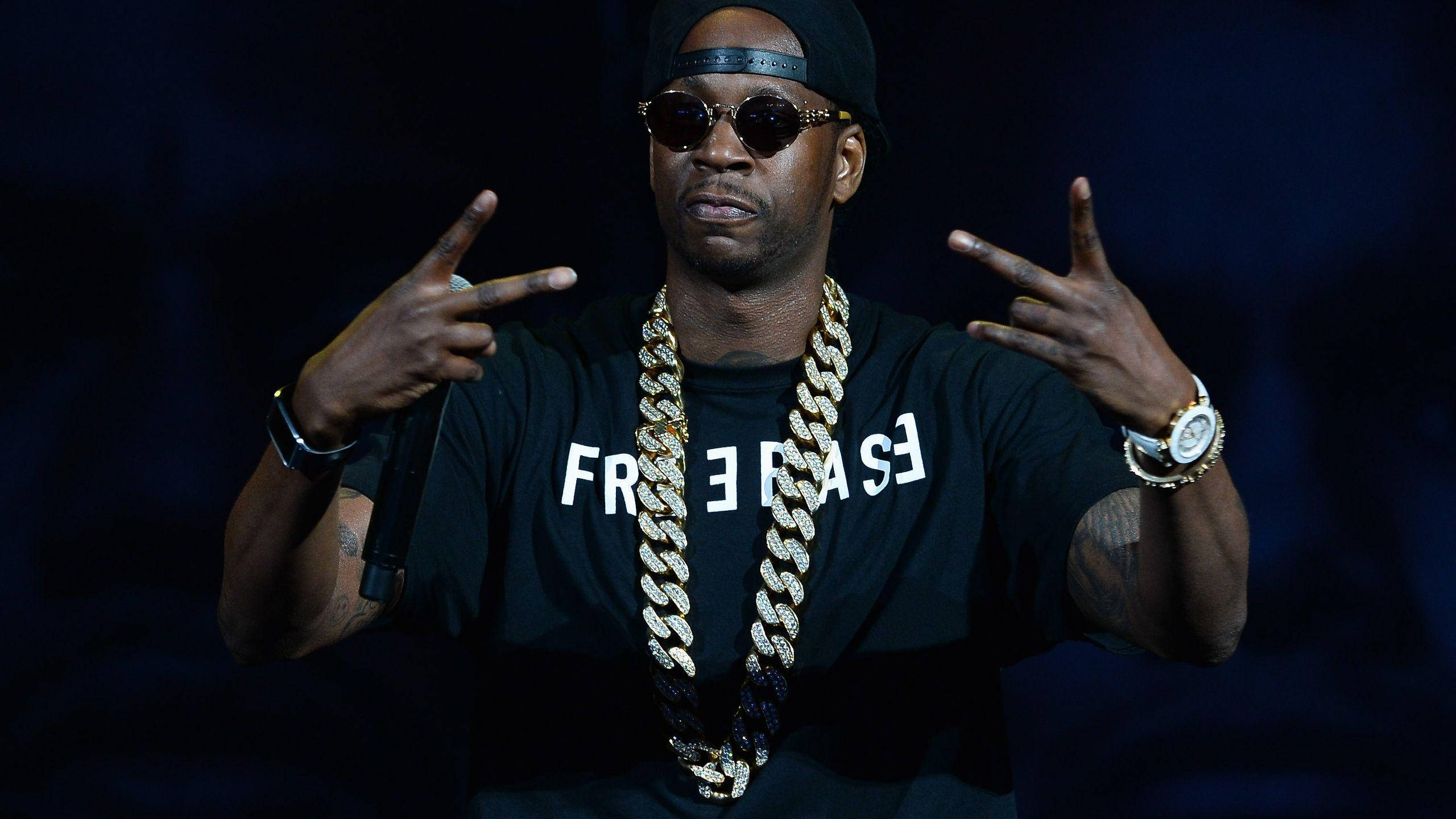 2 Chainz 拉斯維加斯演出 壁紙 — 饒舌歌手Jay-Z在舞台上表演，戴著黑色帽子、太陽眼鏡和一條粗金鏈，同時做出手勢。