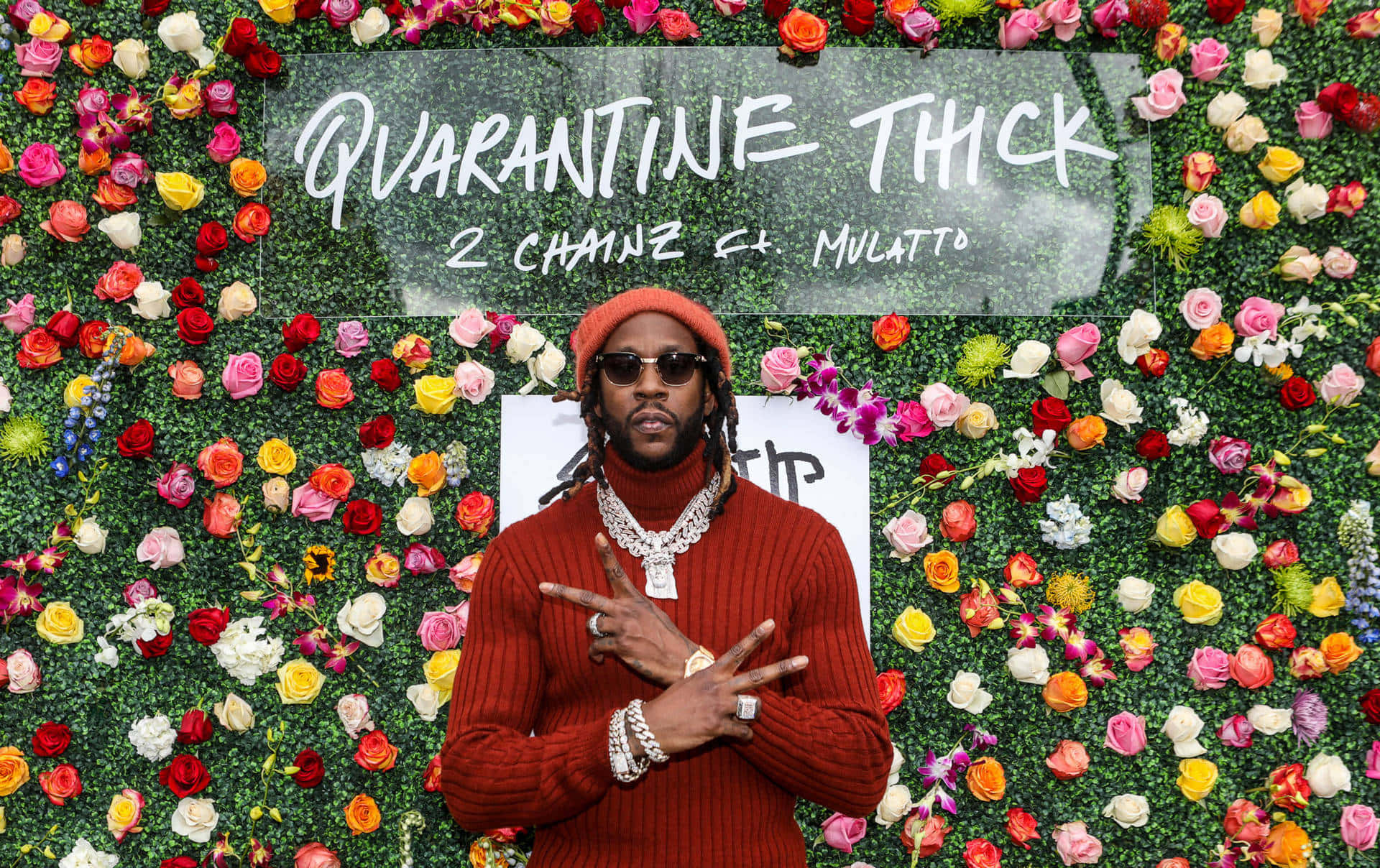 2 Chainz 舞台表演 壁紙 — 身穿紅色毛衣和冷帽的男子自信地站在充滿活力的花卉牆前，牆上寫有 'QUARANTINE THICK' 字樣。
