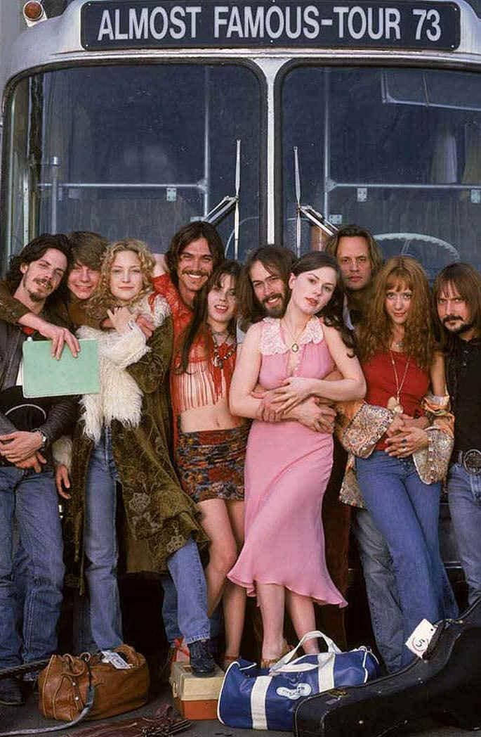 2000年電影《 Almost Famous 》 壁紙 — 一群1970年代的嬉皮士在標有「ALMOST FAMOUS-TOUR 73」的旅遊巴士前，帶著復古行李愉快地擺姿勢。