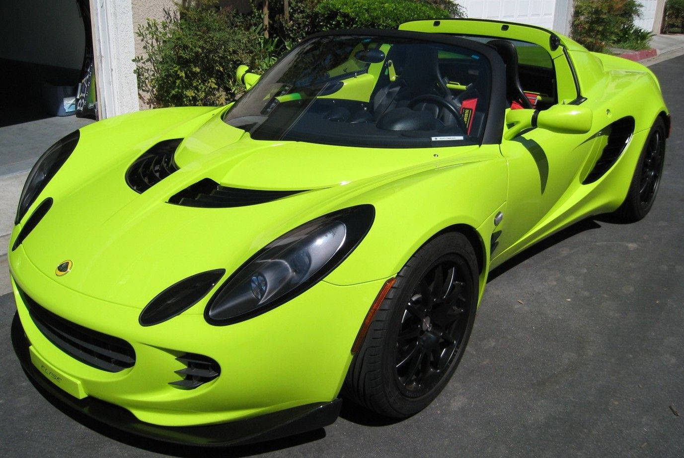 2005款活力檸檬綠蓮花跑車 壁紙 — 一輛充滿活力的青檸綠色蓮花跑車，帶有黑色飾邊，在明亮的日光下停泊在車道上。