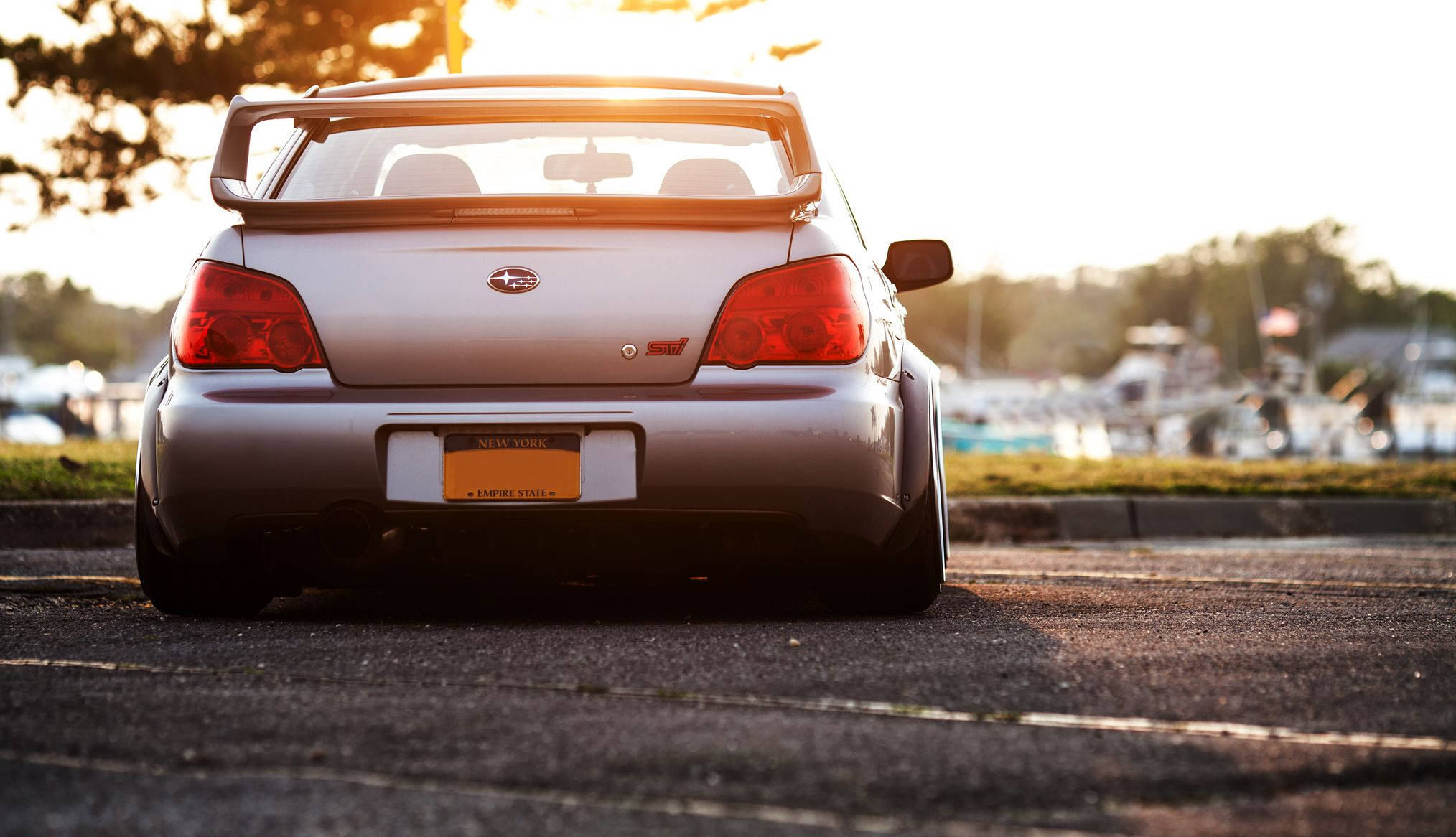 2005銀色斯巴魯Impreza STI 壁紙 — 一架銀色Subaru WRX STI停泊在瀝青路上，金色夕陽在其後方投下長長的影子。