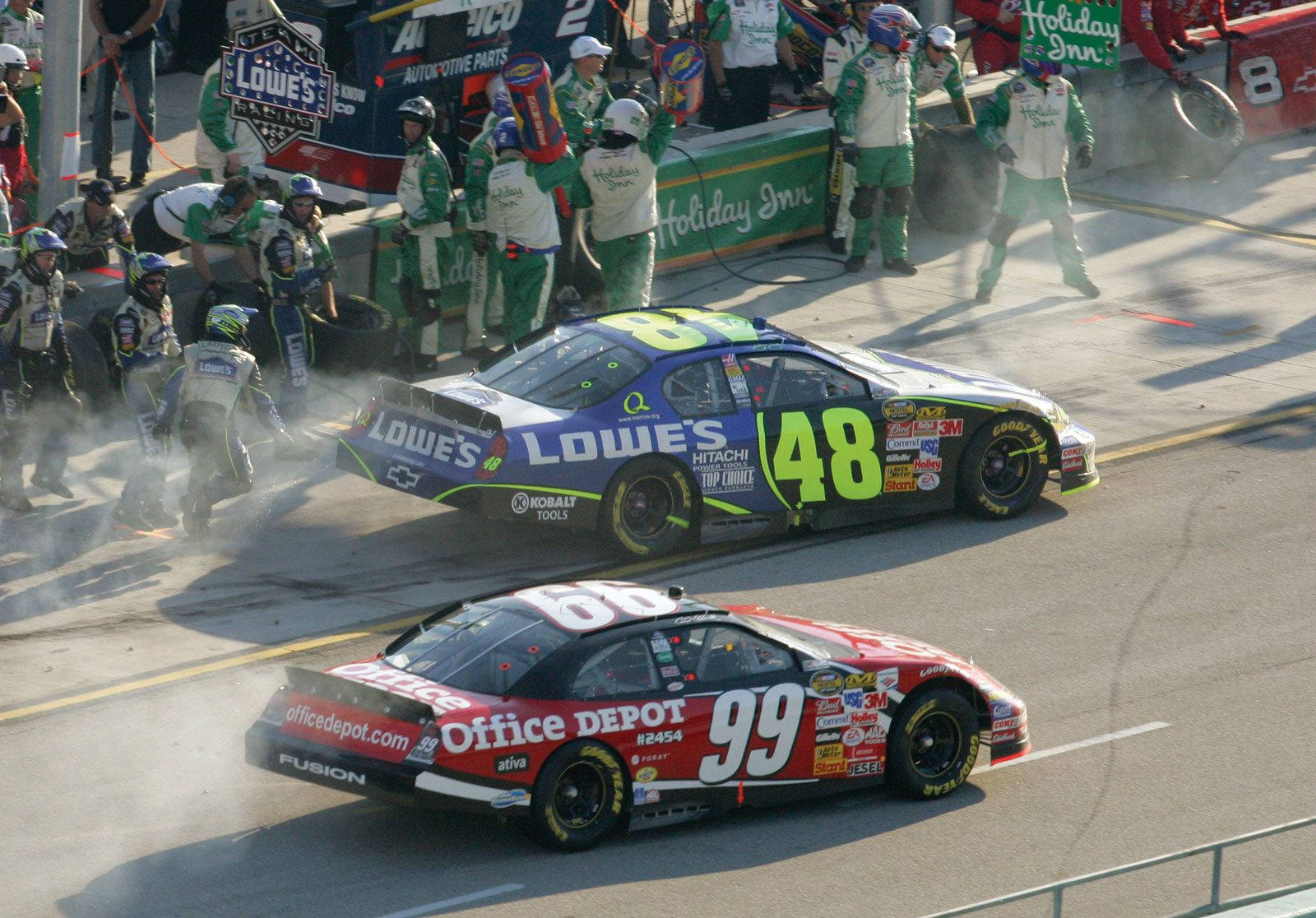 NASCAR賽車在日落時分的維修站停靠中高速駛過維修站工作人員。
