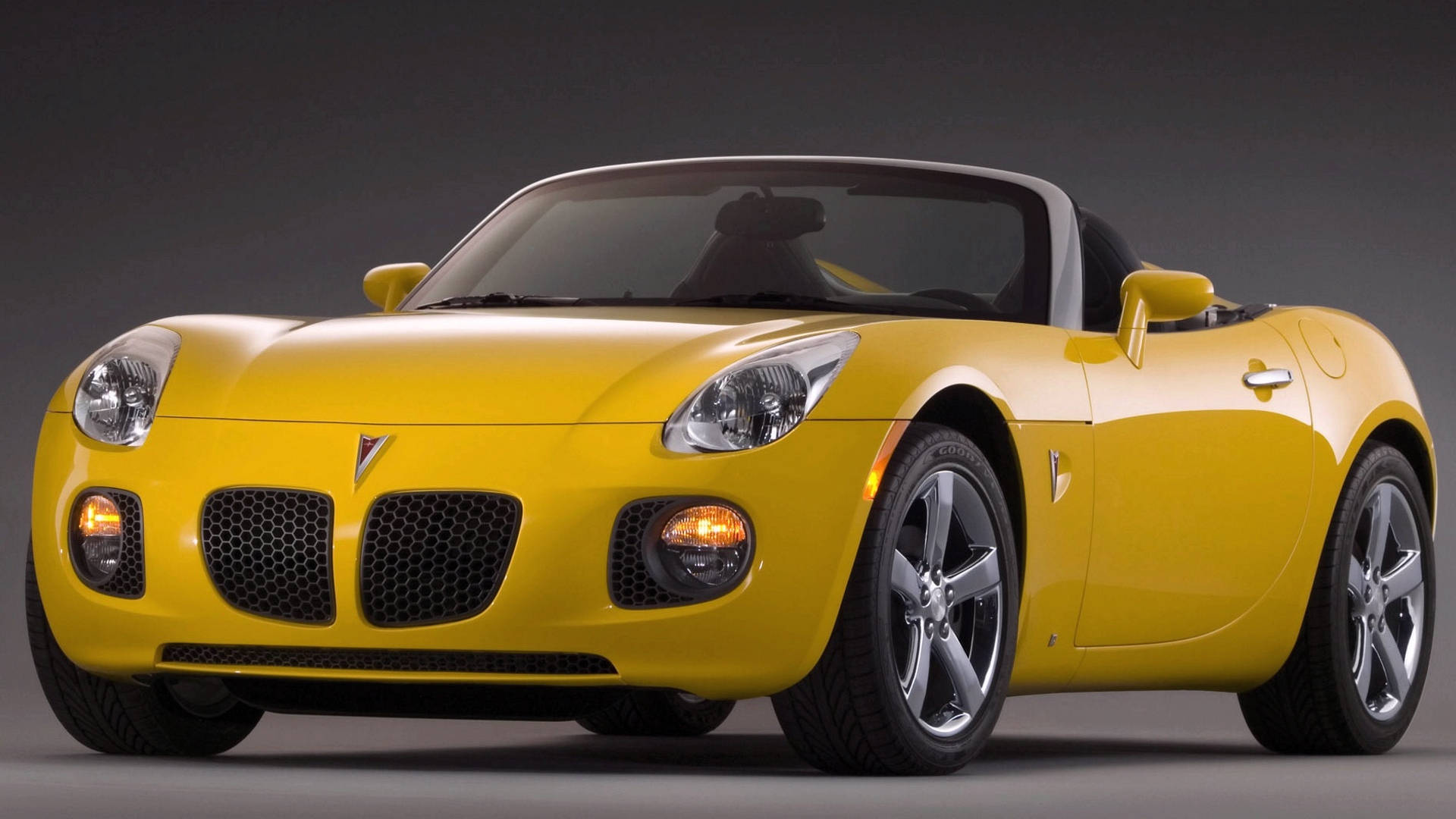 2007 普利茅斯 Solstice GXP 靜態外觀 壁紙 — 一輛充滿活力的黃色Pontiac Solstice開篷跑車，擁有流暢曲線和銀色合金輪圈，在深色工作室背景下擺拍。