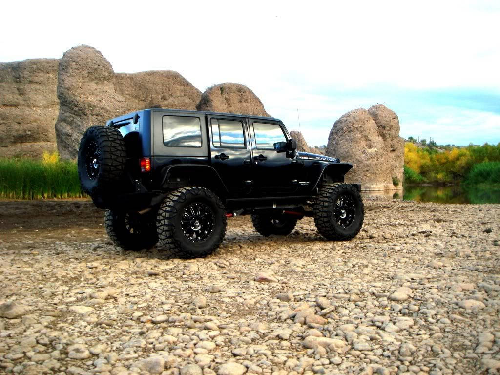 黑色升高Jeep Wrangler泊喺岩石河岸，有砂岩地貌同秋天樹木。