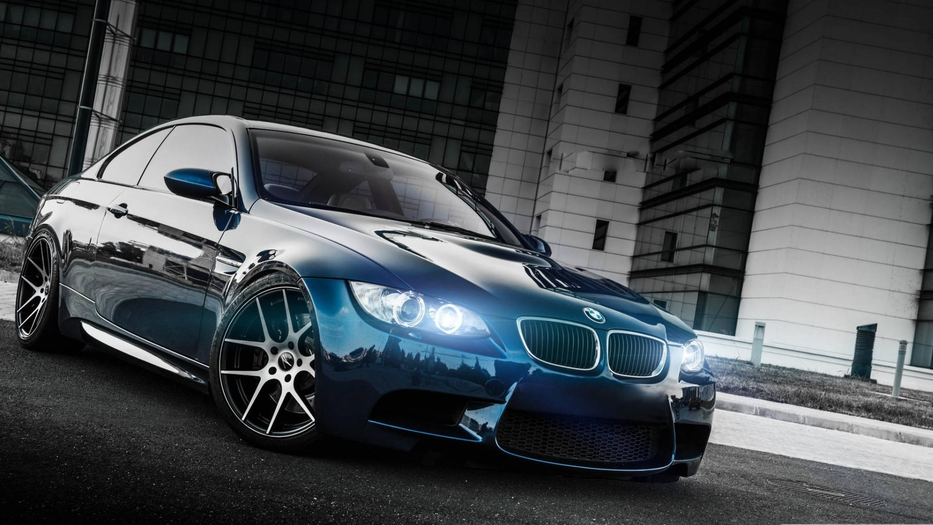 2008 年藍色 BMW M3 全高清 壁紙 — 一輛時尚的藍色BMW M3轎跑車在城市燈光下閃耀，帶有鍍鉻飾邊和發光的車頭燈，背景是單色城市景觀。
