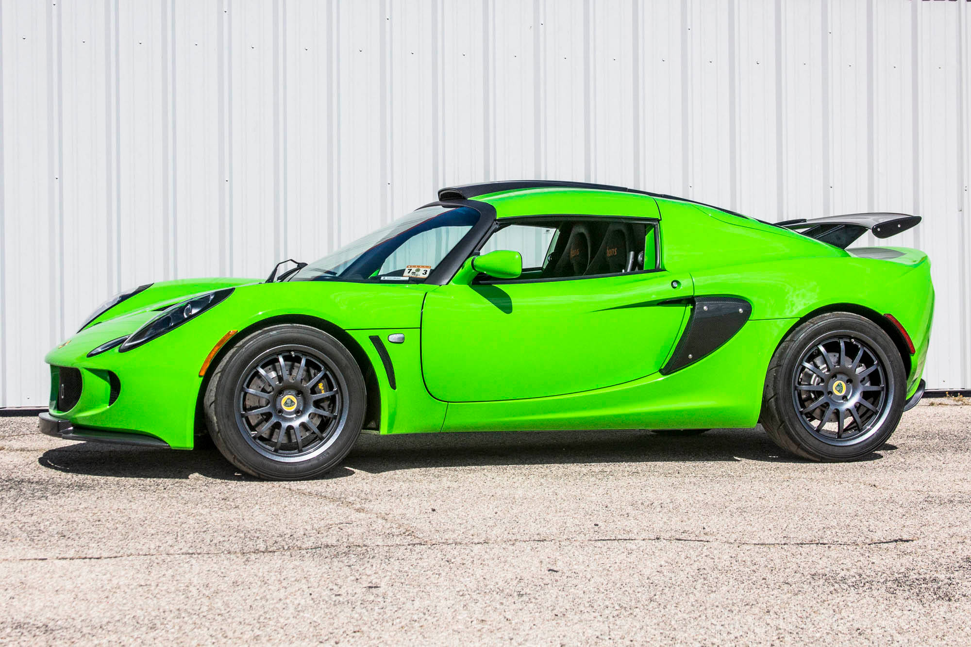 2009年蓮花Exige S 260運動跑車 壁紙 — 一輛充滿活力的青檸綠色蓮花跑車，帶有黑色飾件和後擾流板，停在瀝青路面上，背景是波紋金屬牆。