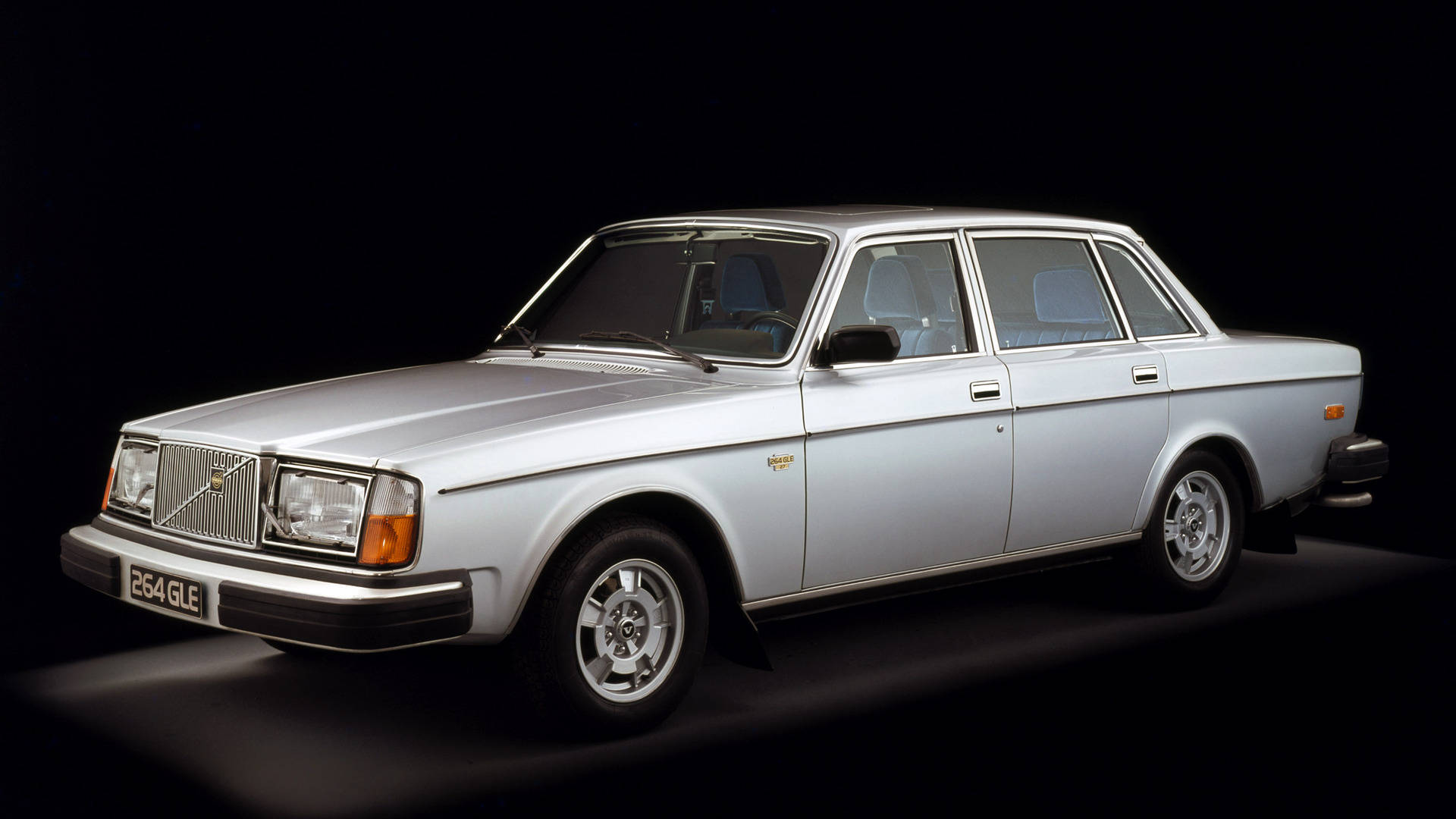 白色200系列Volvo iPhone相片 壁紙 — 一輛時尚的銀色富豪 264 GLE 轎車在黑色背景的戲劇性攝影棚照中展示，配有聚光燈。