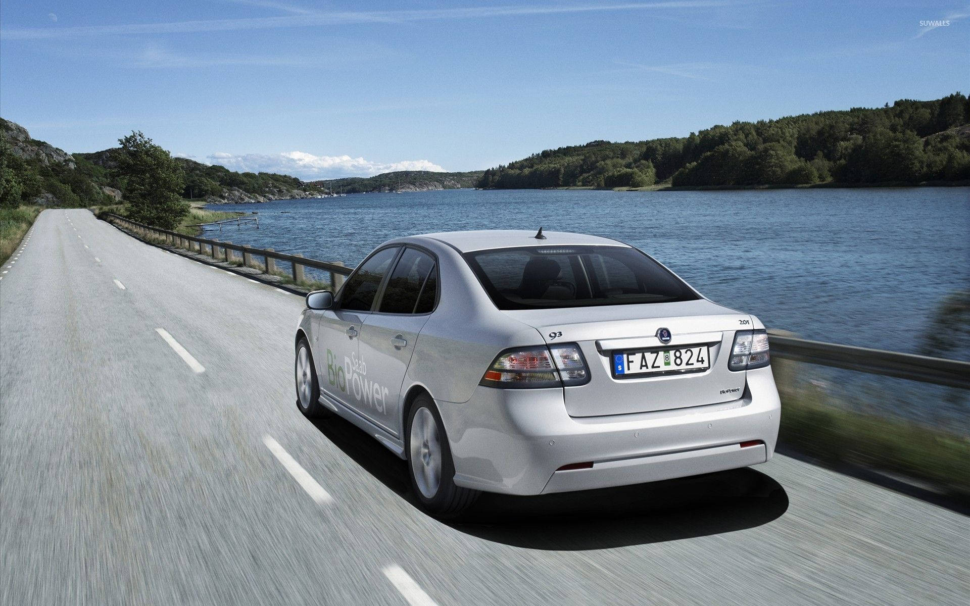 2010 銀色 Saab 9-3 壁紙 — 一架銀色薩博9-3沿著海岸道路行駛，旁邊是平靜的藍色湖泊，天空晴朗。