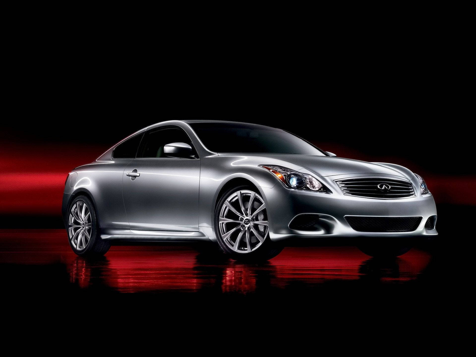 2010 英菲尼迪 G37 Coupe 壁紙 — 一輛時尚的銀色運動轎跑車在黑色背景和反光地板上，在戲劇性的紅色燈光下閃閃發光。