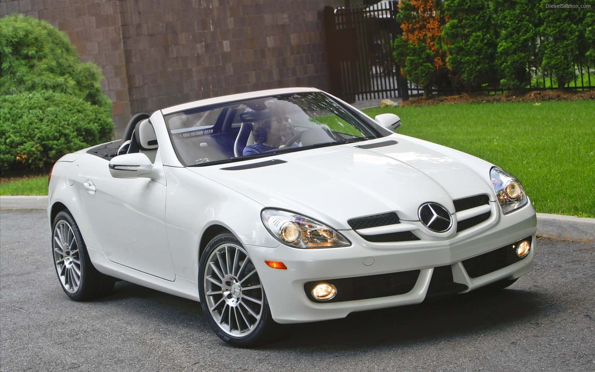 白色平治 SLK 開篷車停泊在車道上，有綠色草坪和樹木。