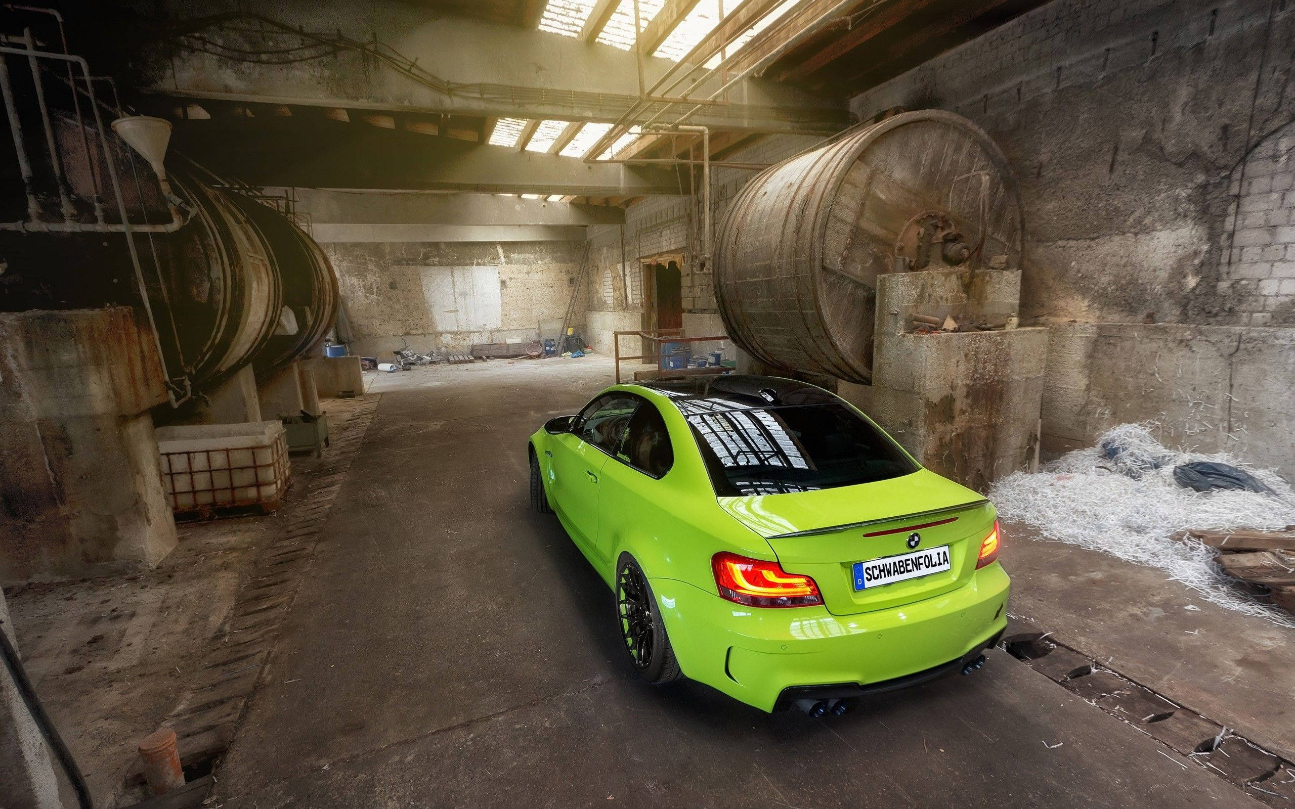 2011 BMW M系列跑車 壁紙 — 一輛充滿活力的青檸綠色BMW M2雙門跑車停放在一個粗糙的工業倉庫中，內有大型生鏽儲罐和天窗照明。