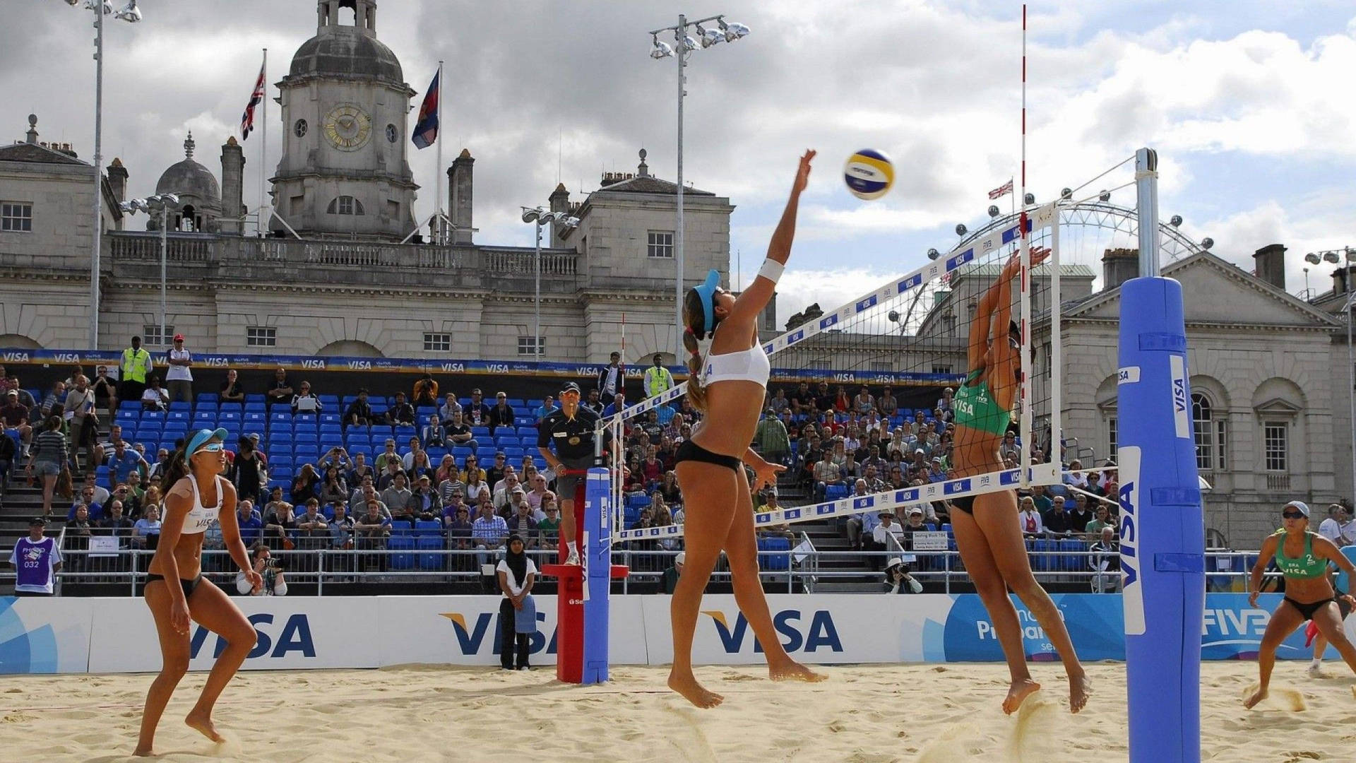 2011 Visa FIVB海灘排球賽倫敦站 壁紙 — 兩名沙灘排球選手高高躍起，將球扣過網，身後是一座宏偉的歷史建築。