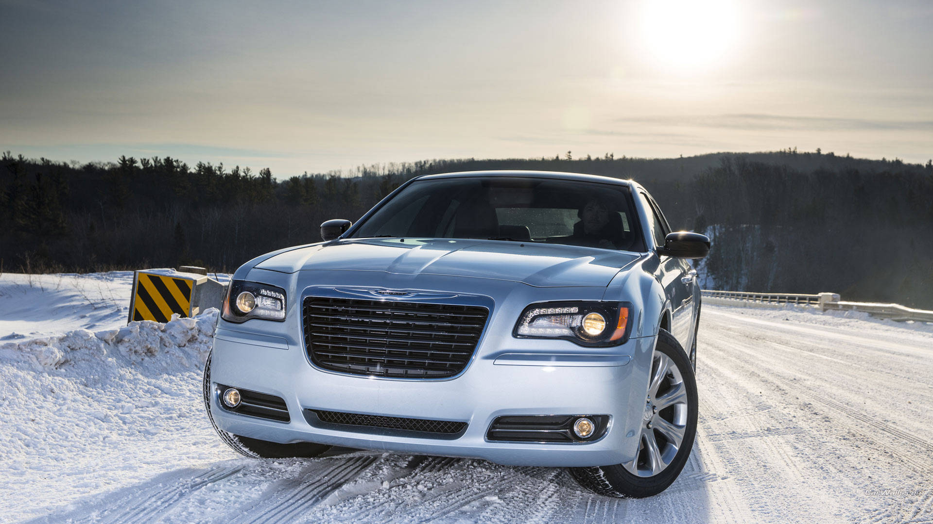 2013 Chrysler 300 壁紙 — 一輛銀色房車在明亮的陽光下行駛在白雪覆蓋的道路上，穿過冬季森林。