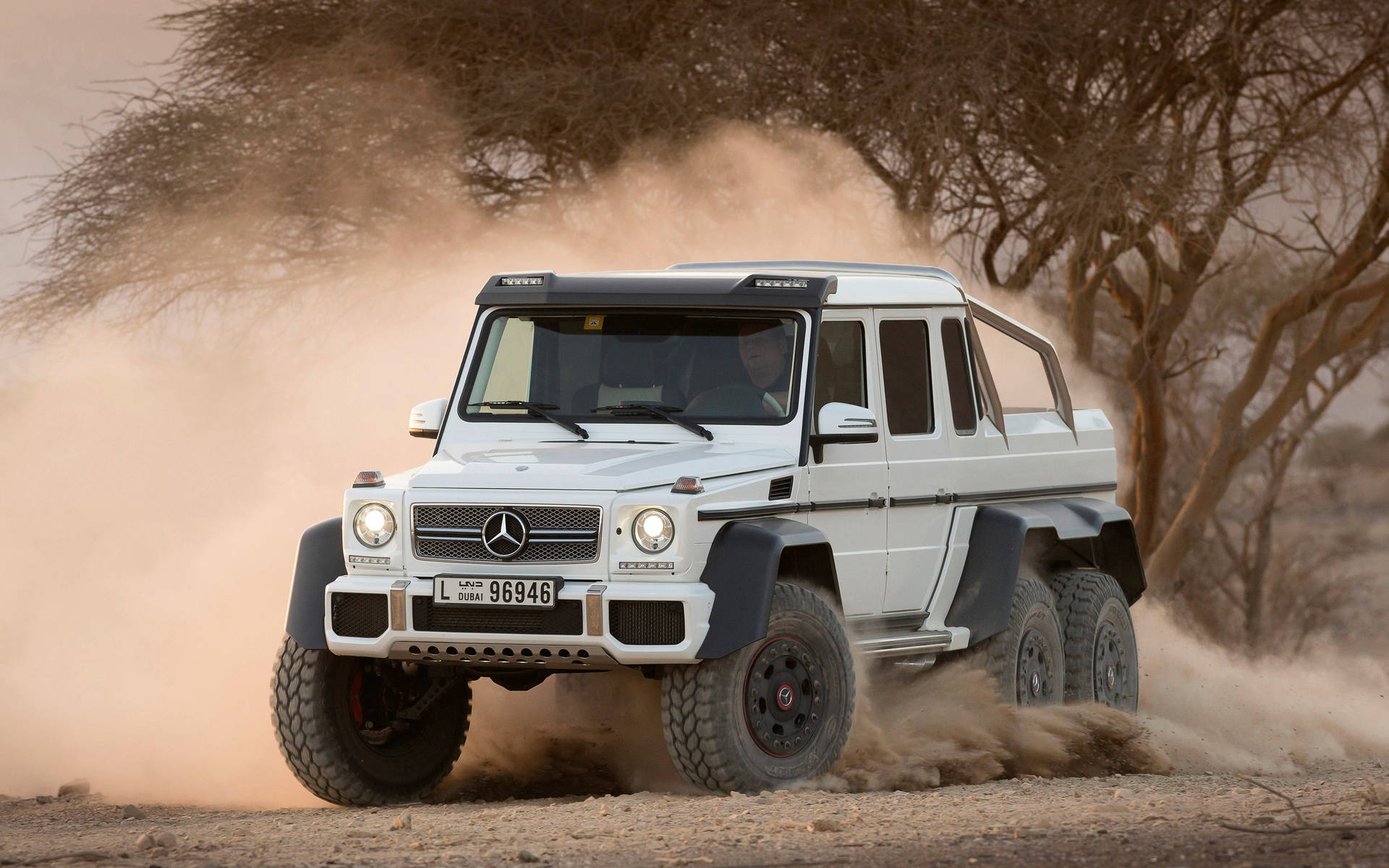 白色Mercedes G63 6x6在塵土飛揚的非洲稀樹草原上行駛。