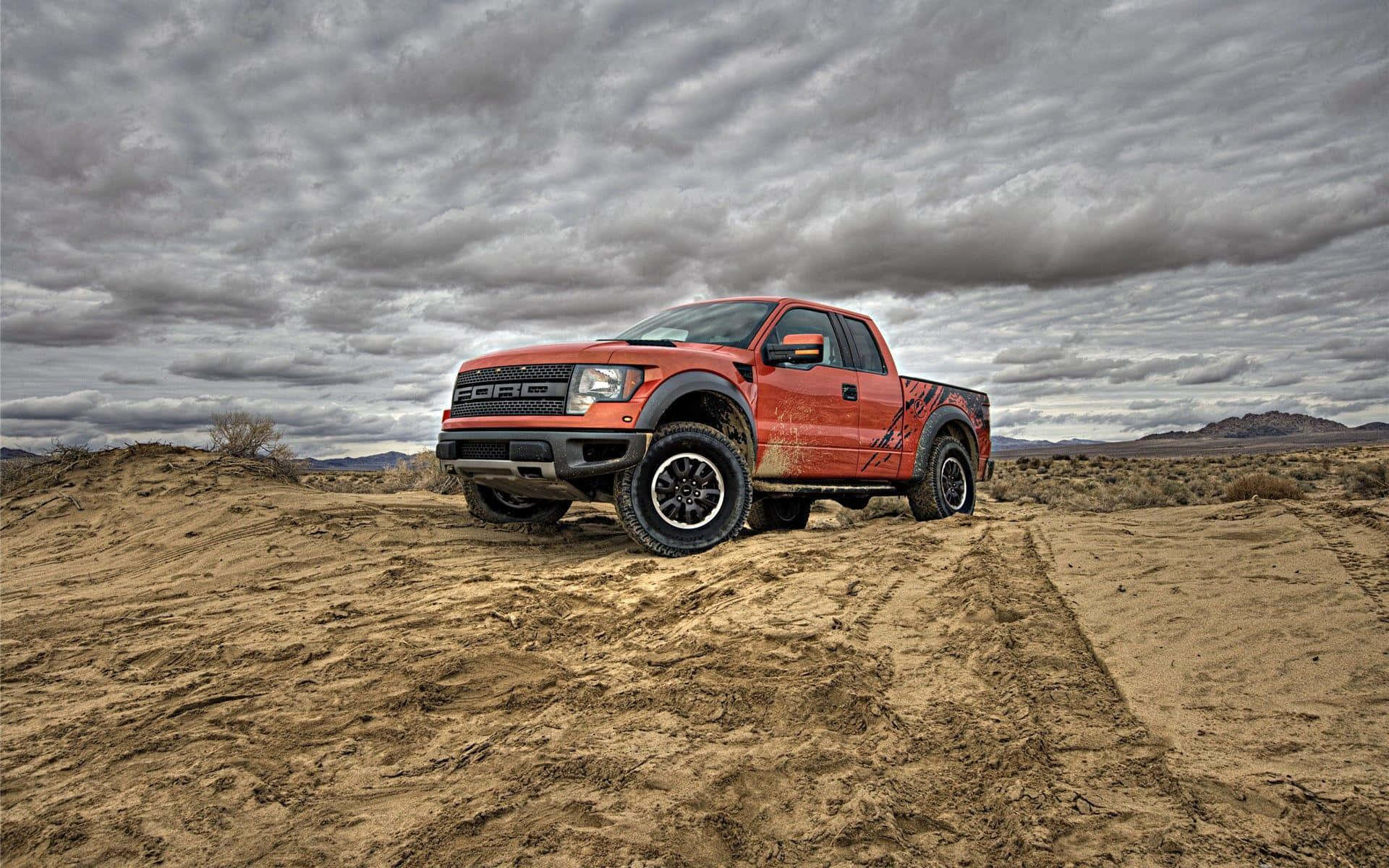 2013款紅色福特F-150 SVT Raptor皮卡 壁紙 — 一架堅固的橙色福特F-150貨車在戲劇性的多雲天空下行駛於塵土飛揚的沙漠景觀中。