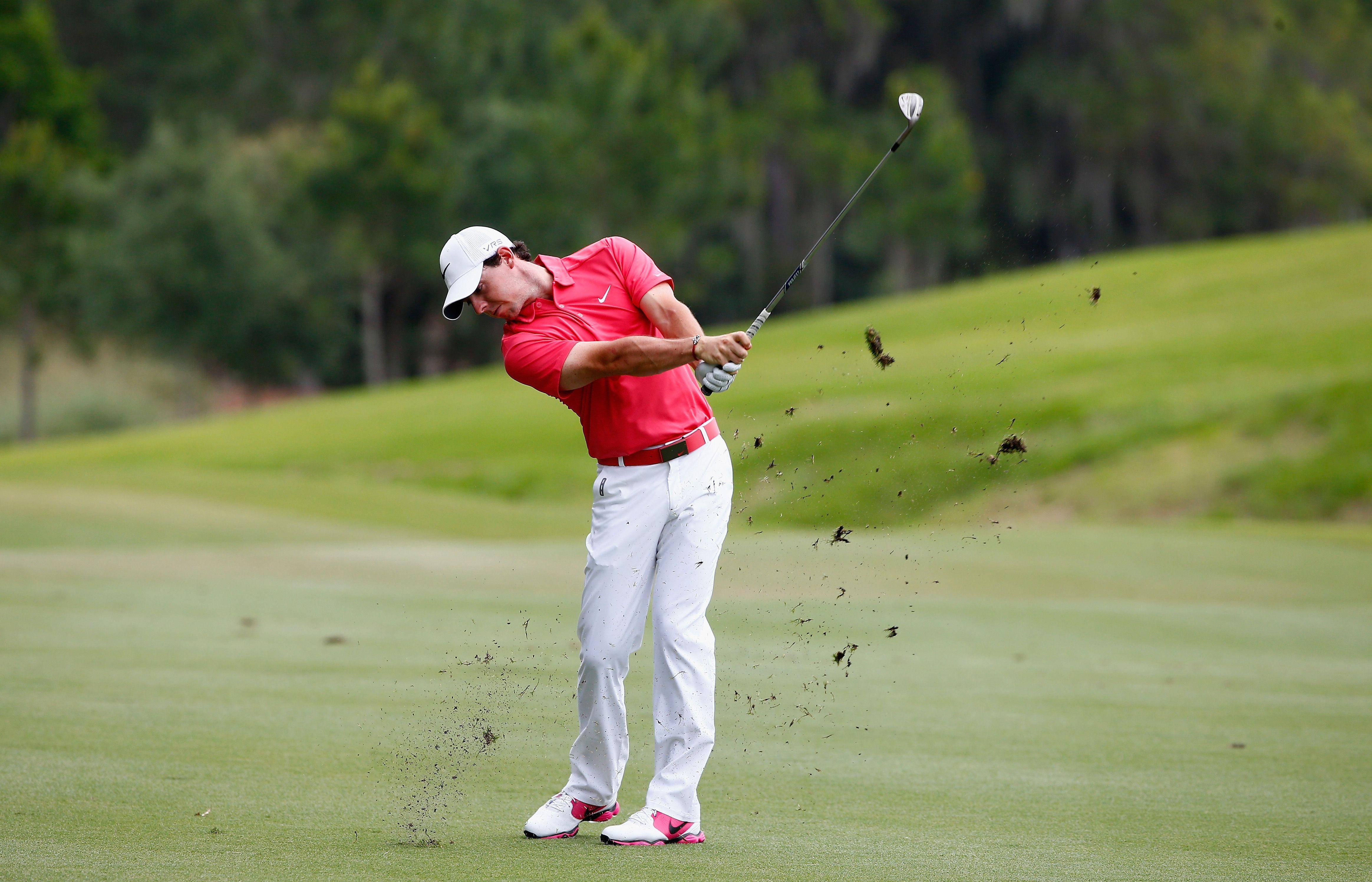 2014 PGA 玩家錦標 麥克羅伊 壁紙 — 一位身穿紅衫白褲的高爾夫球手在翠綠的球場上揮桿，泥土飛揚。