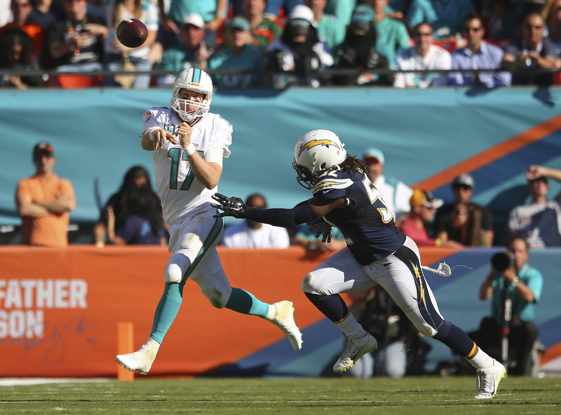 2014年佛羅里達海豚隊對陣聖地牙哥 chargers 田納西泰坦隊瑞安·坦尼爾 壁紙 — 邁阿密海豚隊的四分衛在日間NFL比賽中擲出橄欖球，而洛杉磯電光隊的防守球員跳起嘗試攔截。