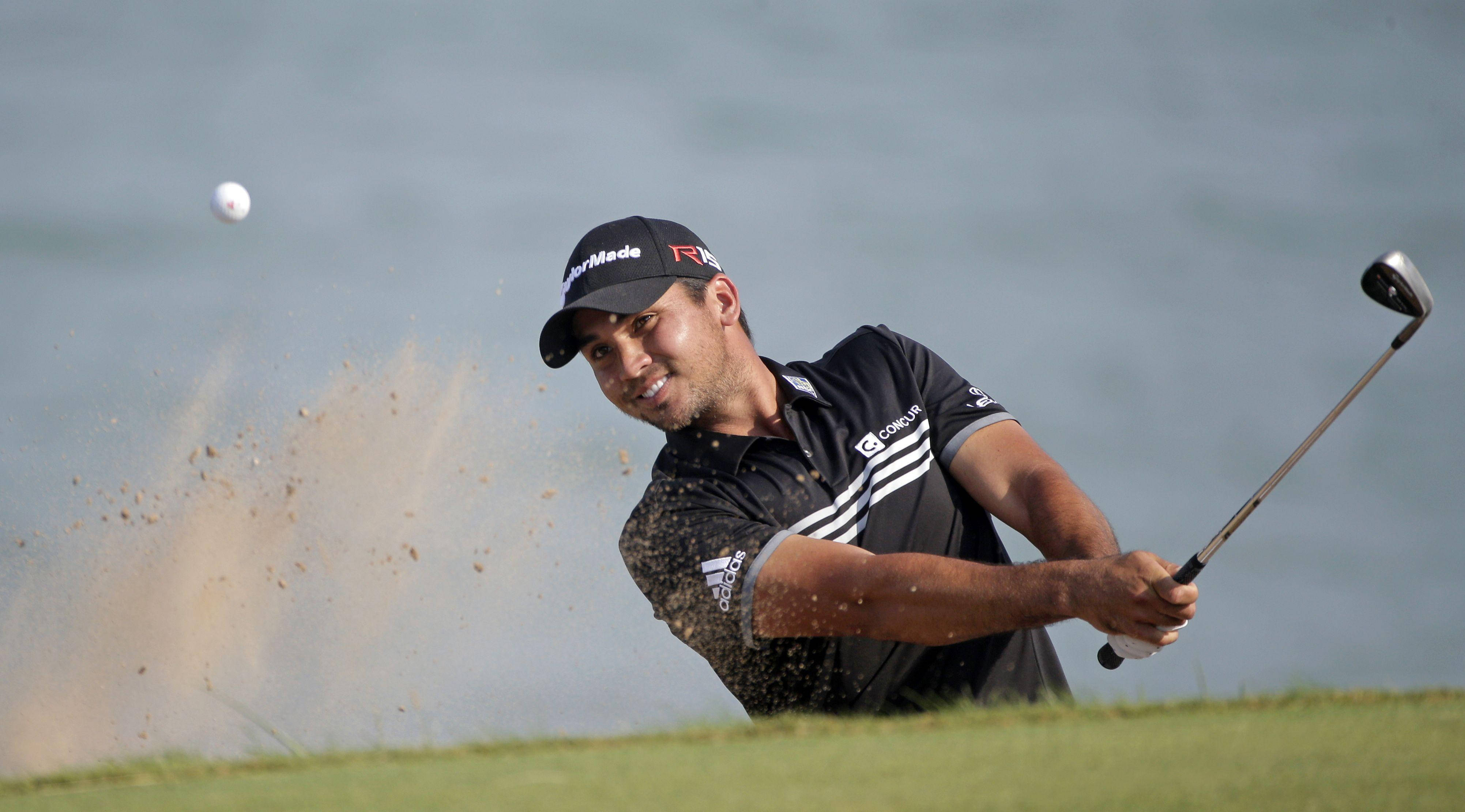 2015 PGA 比賽 杰森·戴 壁紙 — 高爾夫球手從沙坑揮桿，將沙塵揚起，專注表情，背景是模糊的水面。