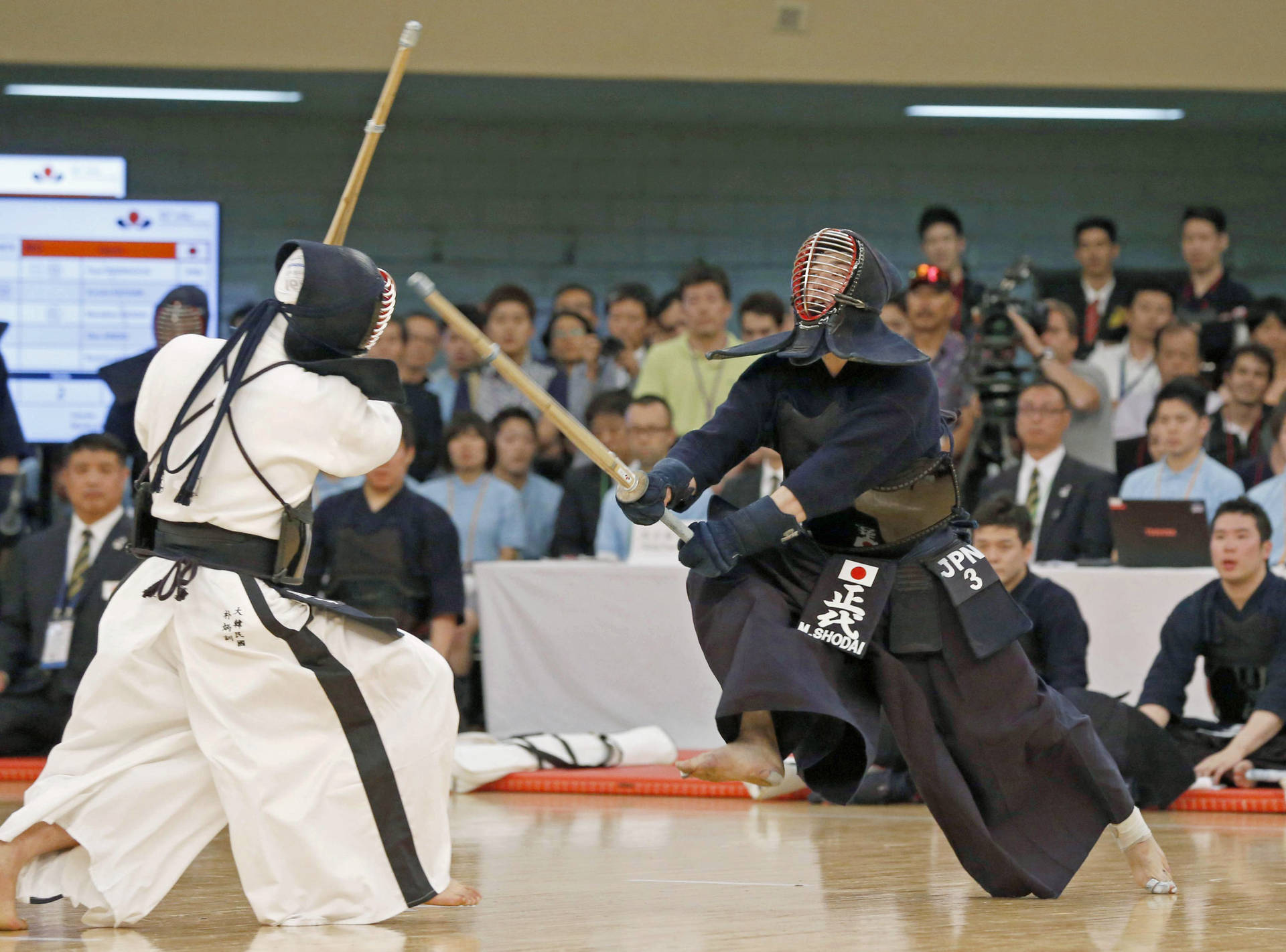 2015年世界劍道錦標賽 Masahiro Shodai衝刺對決 壁紙 — 兩名全副武裝的劍道鬥士在觀眾面前用竹劍進行緊張的室內比賽。