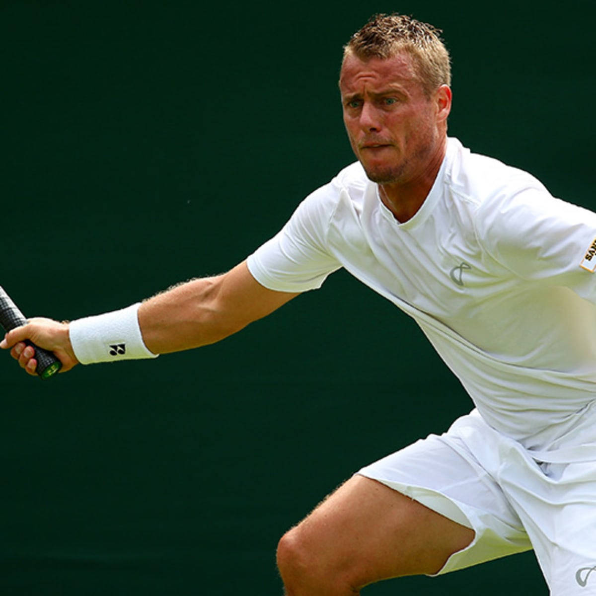 2015年溫布頓錦標賽 Lleyton Hewitt 壁紙 — 一名身穿白色裝備的男性網球選手，在深綠色背景下，帶著強烈的專注力向前猛衝。