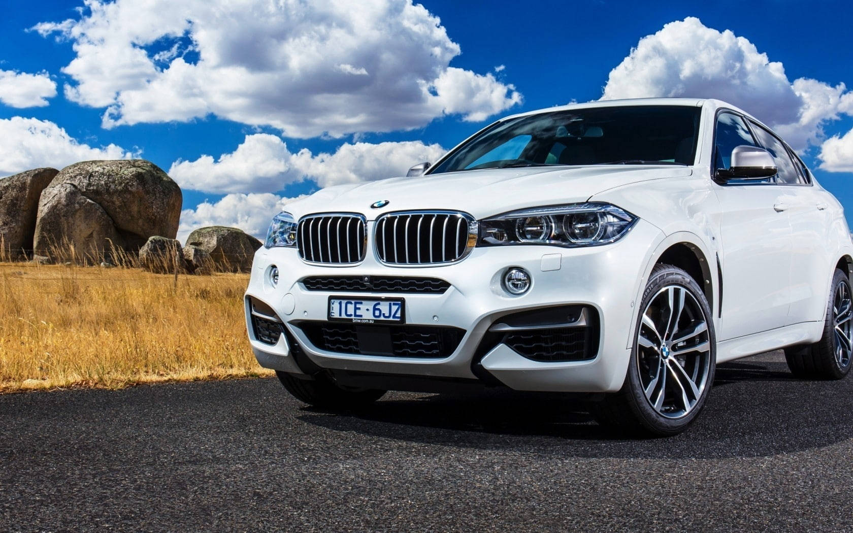 2015款白色BMW X6 M雲景 壁紙 — 一輛純白色的BMW X5 SUV停泊在瀝青路上，背景是湛藍的天空、蓬鬆的白雲和巨大的岩石。