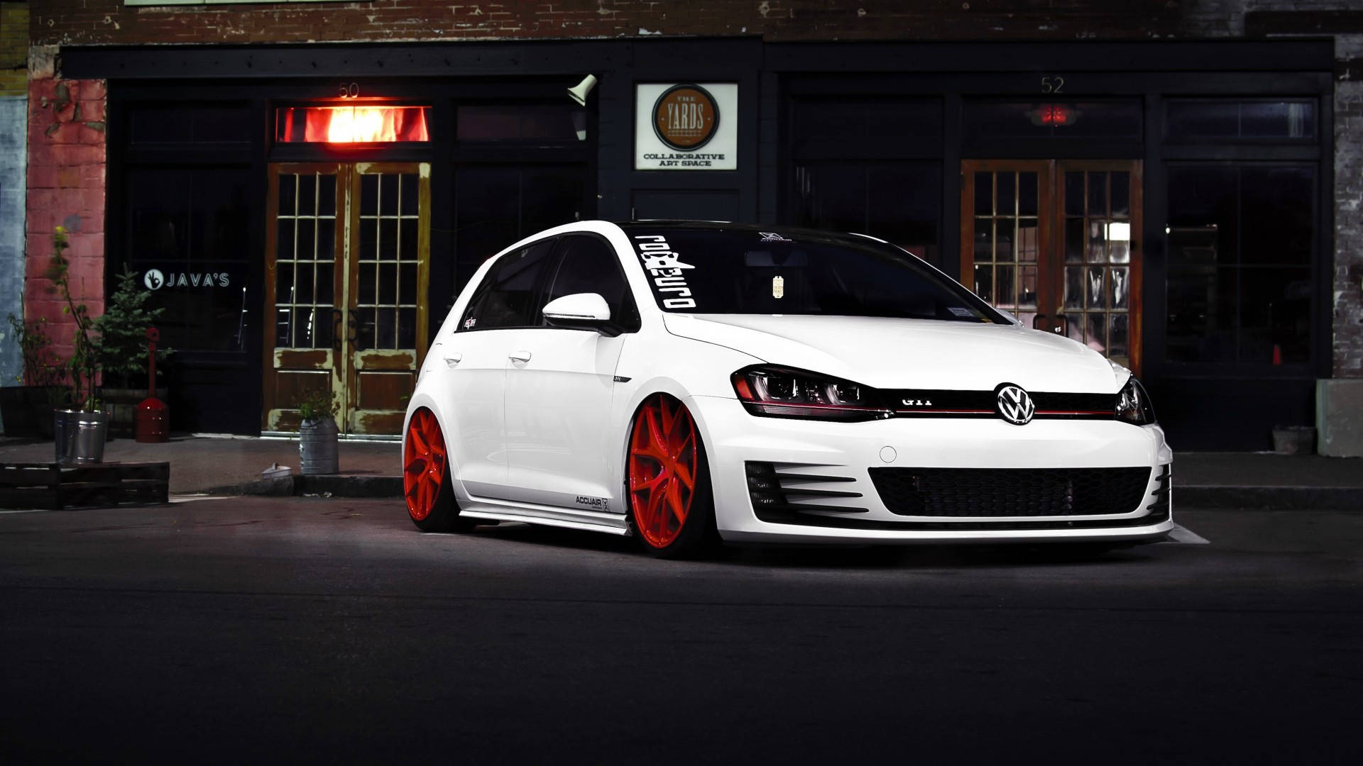 2015款白色Volkswagen Golf GTI 壁紙 — 一輛白色福士Golf配以鮮紅色輪圈，夜間停泊在帶有發光招牌的磚砌建築前。