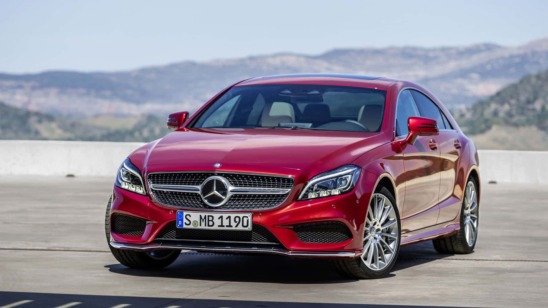 紅色 Mercedes-Benz CLS Coupe 停放在陽光明媚的觀景台上，背景有山脈。