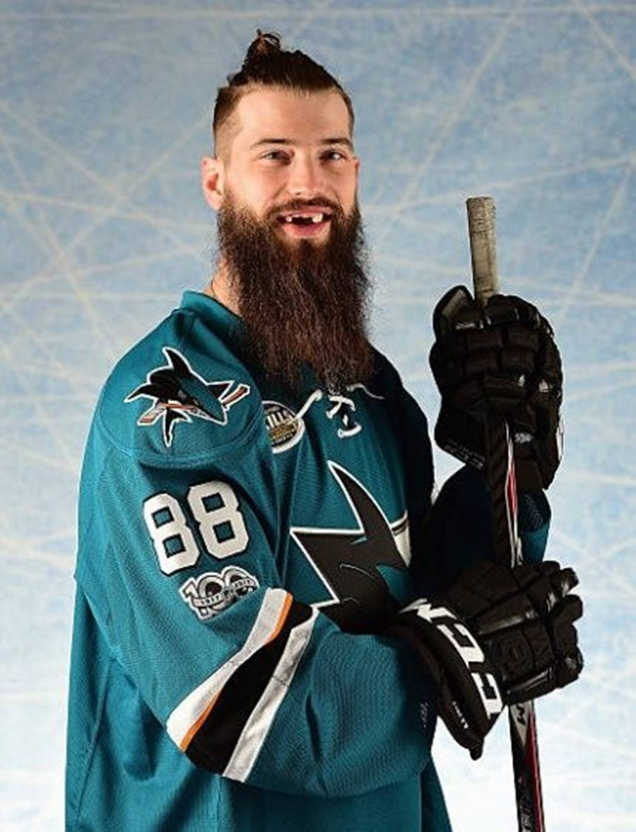 布倫特·伯恩斯2017年本田NHL全明星賽 壁紙 — 一位留鬍子的曲棍球運動員，身穿青色鯊魚隊88號球衣，在冰場背景下微笑著拿著球桿。