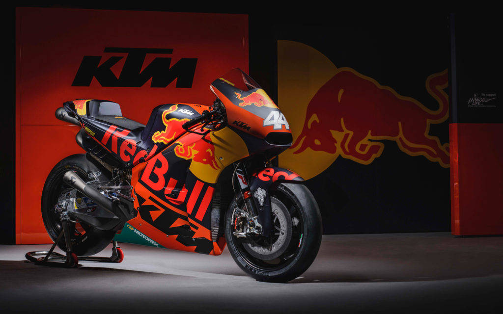 2017年MotoGP賽事中的紅牛贊助RC17 KTM賽車 壁紙 — 一輛帶有Red Bull塗裝的KTM MotoGP賽車，在工作室環境中放在支架上，背景是品牌牆壁。