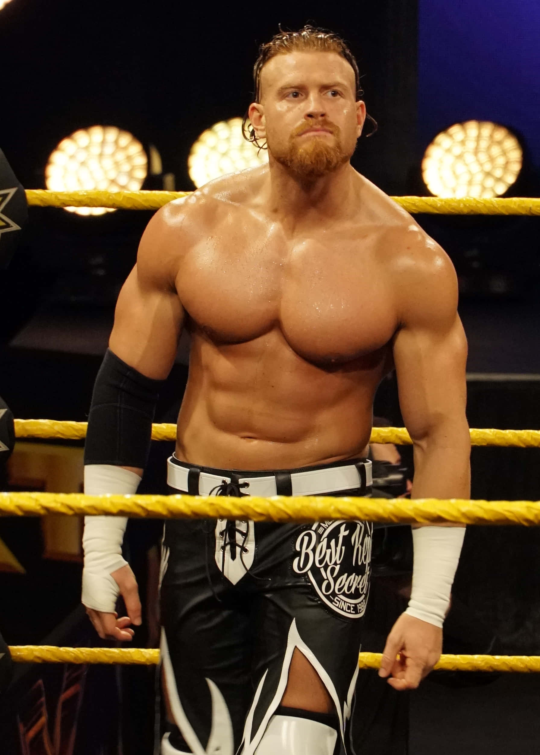 巴迪·墨菲 2018 WWE活動 壁紙 — 一位肌肉發達、留鬍子的摔角手在明亮的場館燈光下自信地站在摔角台上。