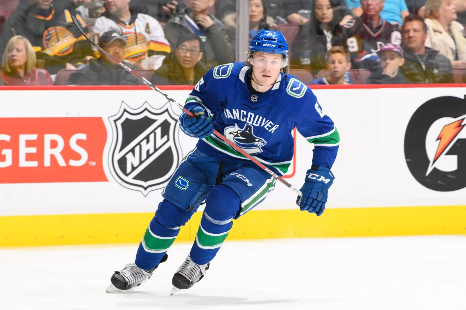 2018年NHL賽事中專注的布洛克·布瑟 壁紙 — 一名身穿藍綠色裝備的溫哥華加人隊冰球球員在冰上激烈滑行，背景有觀眾。