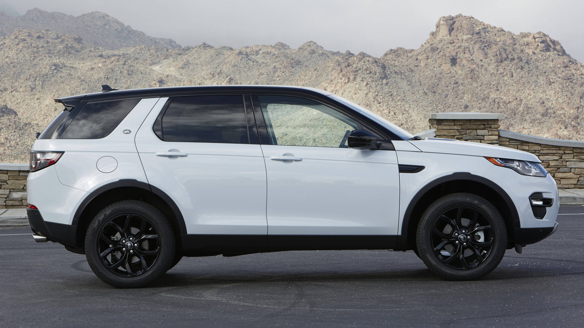 2018款白色路虎 iPhone 主題壁紙 壁紙 — 一輛時尚的白色 Land Rover Discovery Sport 帶有黑色飾邊，停在瀝青路面上，背景是崎嶇的沙漠山脈。