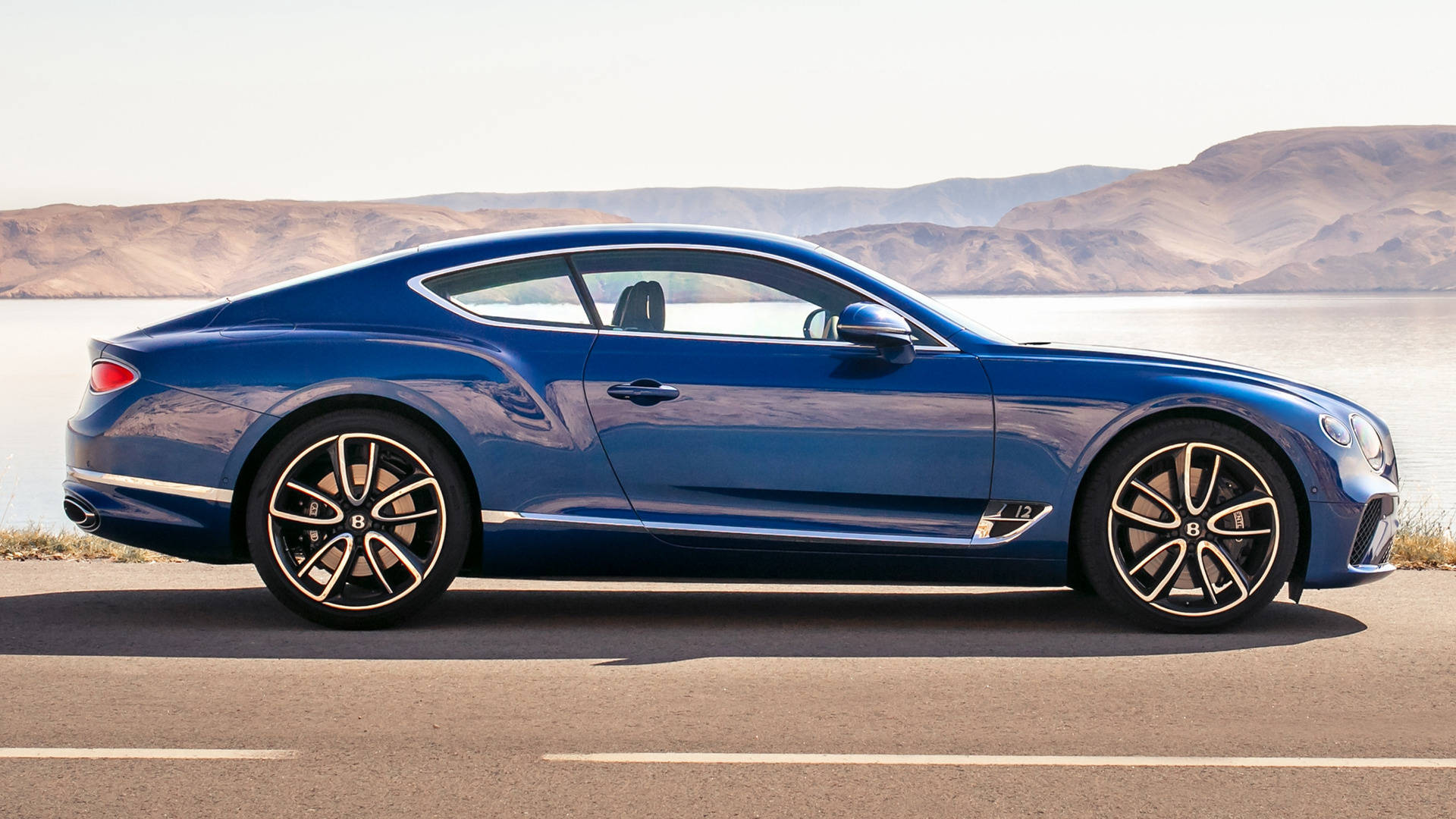 藍色 Bentley 跑車停泊在湖邊，遠方有山脈。