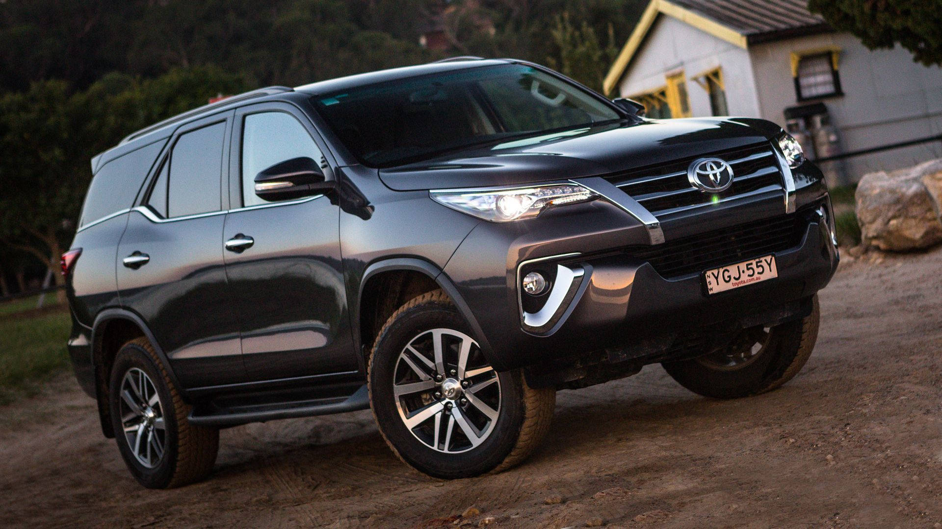 2019 BS 6款豐田Fortuner 壁紙 — 一輛時尚的黑色豐田SUV停泊在房屋附近的泥路上，背景有樹木。