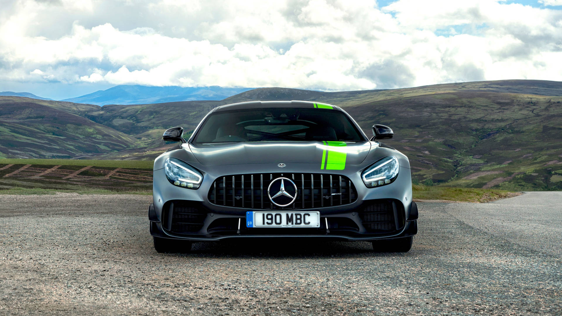 銀色 Mercedes-AMG GT 跑車在碎石路上，有山丘和雲朵。