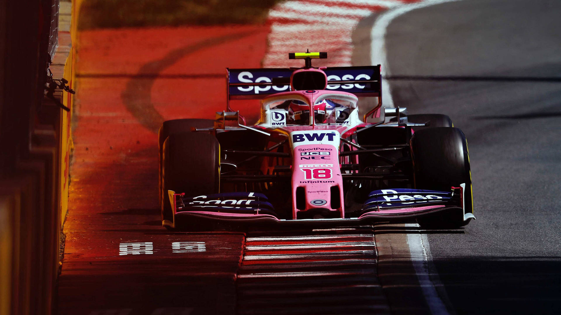 粉紅色和黑色的 Formula 1 賽車在夜間於燈光照亮的賽道上飛馳。