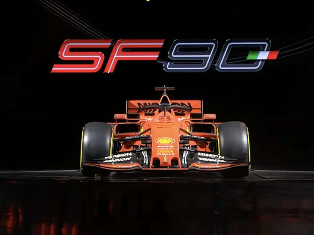 2019年法拉利SF90一級方程式賽車發表日 壁紙 — 一輛充滿活力的橙色一級方程式賽車SF90在黑暗的舞台上展示，上方有發光的標誌，燈光效果戲劇化。