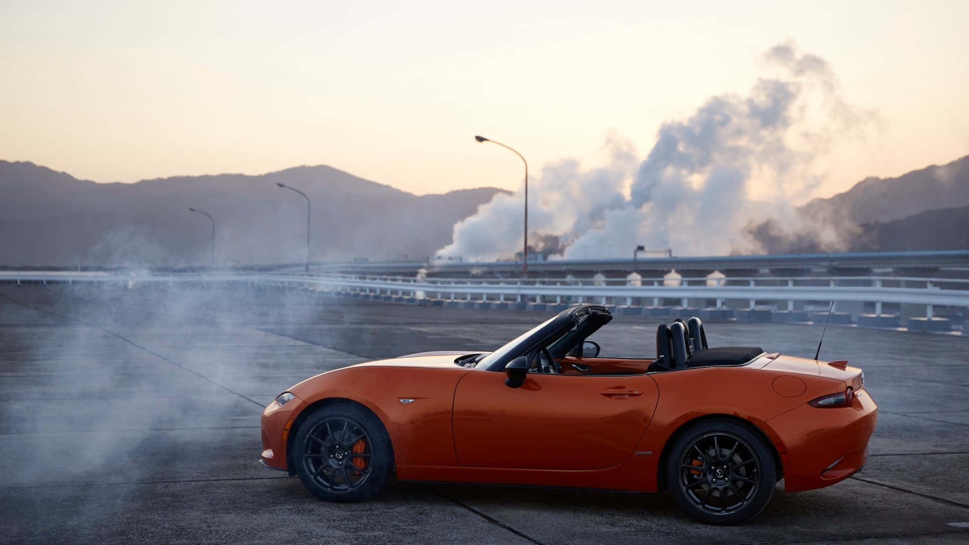 2019年馬自達MX-5 Miata側面視角 壁紙 — 一輛充滿活力的橙色開篷跑車在日落時分的高速公路上飄移，身後煙霧滾滾。