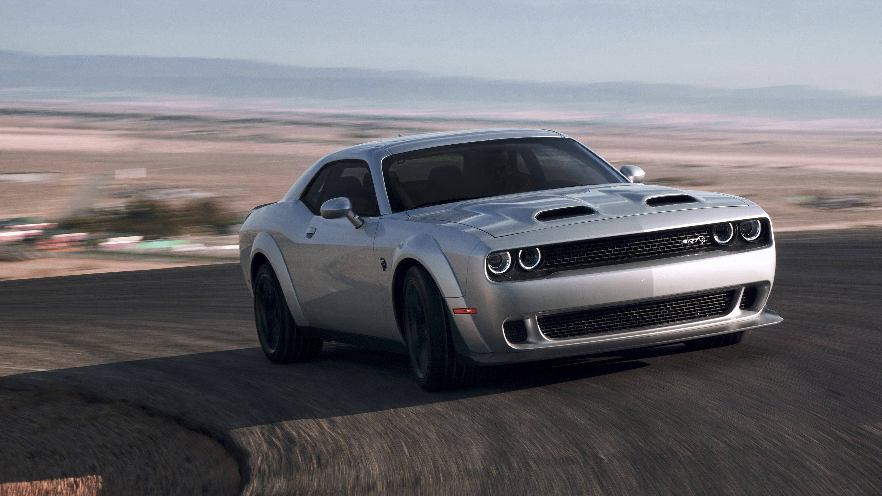 2019款道奇挑戰者SRT Hellcat 壁紙 — 一輛銀色Dodge Challenger SRT Hellcat在沙漠公路上疾馳，周圍景物模糊。