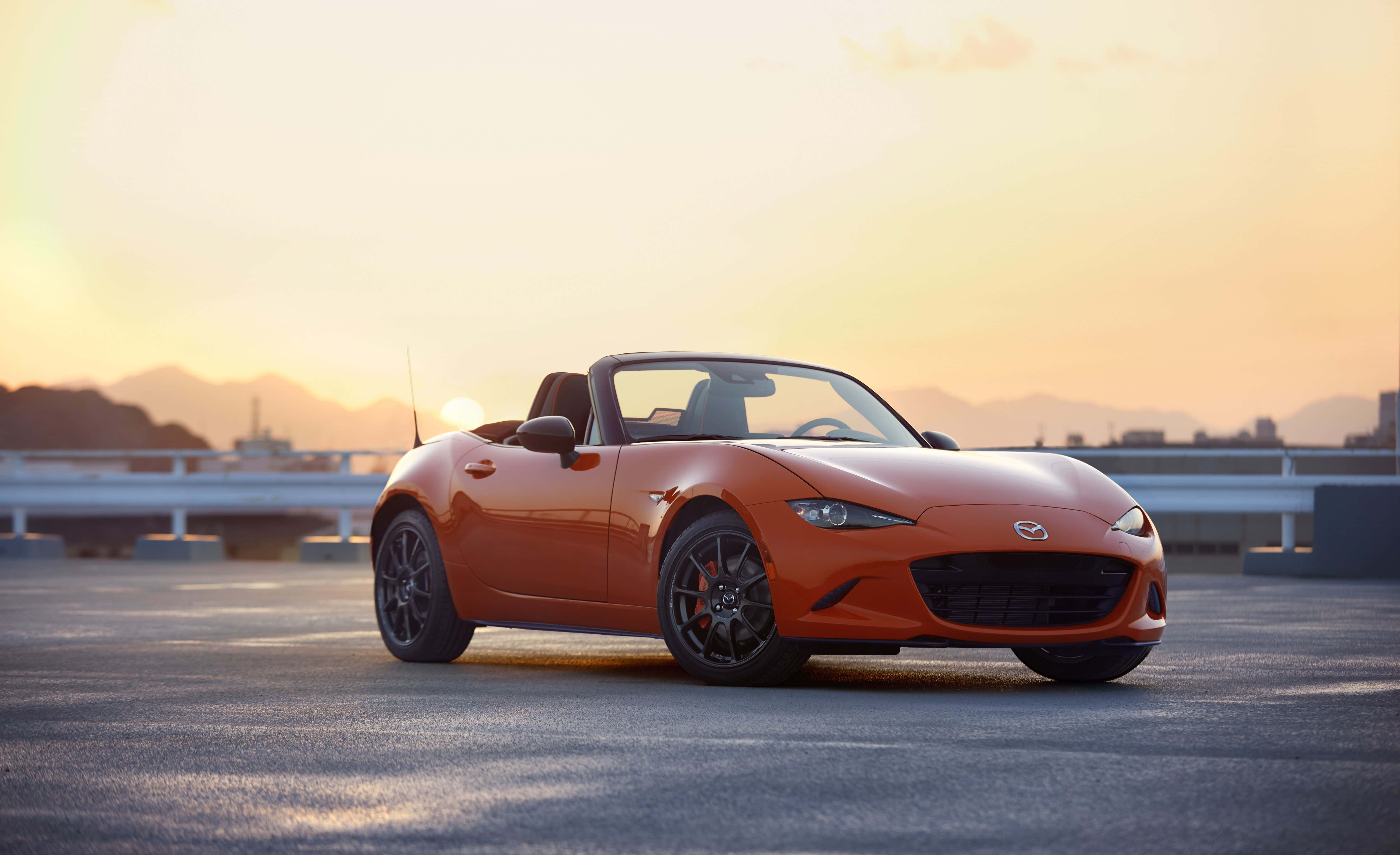 2019款馬自達MX-5 Miata橙色運動跑車 壁紙 — 一輛充滿活力的橙色萬事得MX-5 Miata開篷跑車停泊在高速公路天橋上，背景是金色夕陽和遠山。